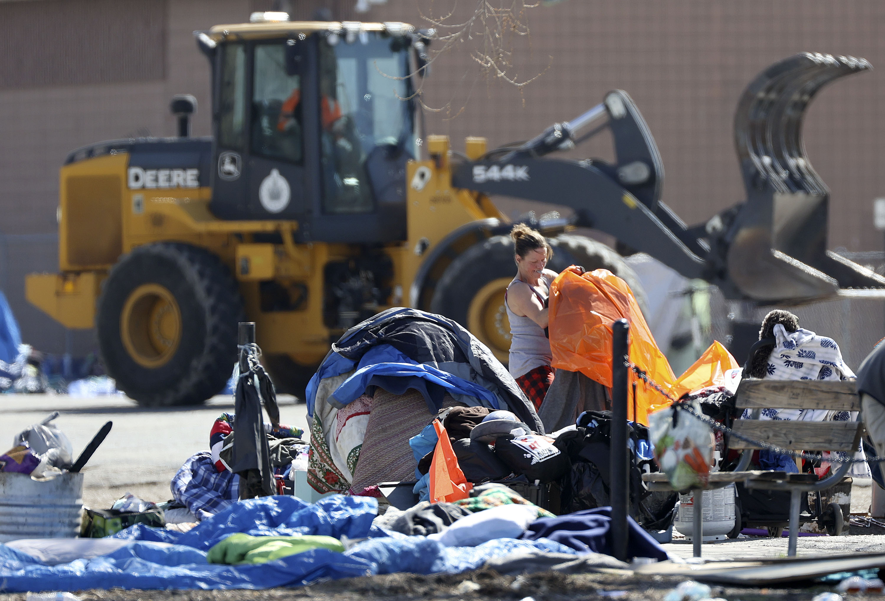Brandie Smith packs up belongings as backhoes pick up remnants of homeless camps and load them into dump trucks near the Rio Grande Depot in Salt Lake City on April 1, 2021. Salt Lake City's director of homelessness said allowing small camps has been one of the city's only options for handling overflow shelter needs during the pandemic.