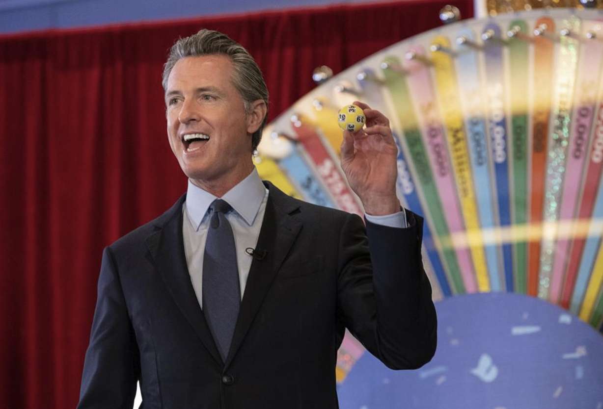 FILE - In this June 4, 2021, file photo, California Gov. Gavin Newsom holds up a lottery ball at the California Lottery Headquarters on Friday, June 4, 2021, in Sacramento, Calif., while drawing numbers for California's new vaccine incentive program. California, the first state in America to put in place a coronavirus lockdown, is now turning a page on the pandemic. Most of California's coronavirus restrictions will disappear Tuesday, June 15, 2021. (Paul Kitagaki Jr./The Sacramento Bee via AP, File)