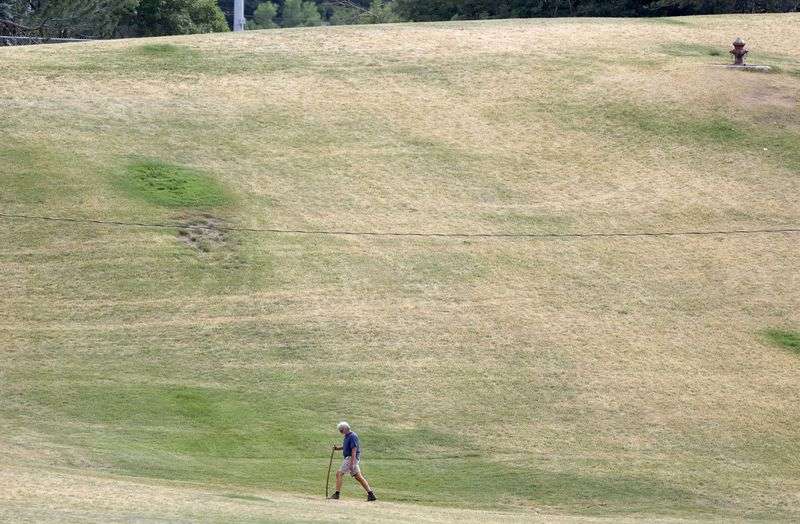 A man walks near a hillside of dry grass in Sugar House Park in Salt Lake City on Wednesday, June 16, 2021, during a drought.