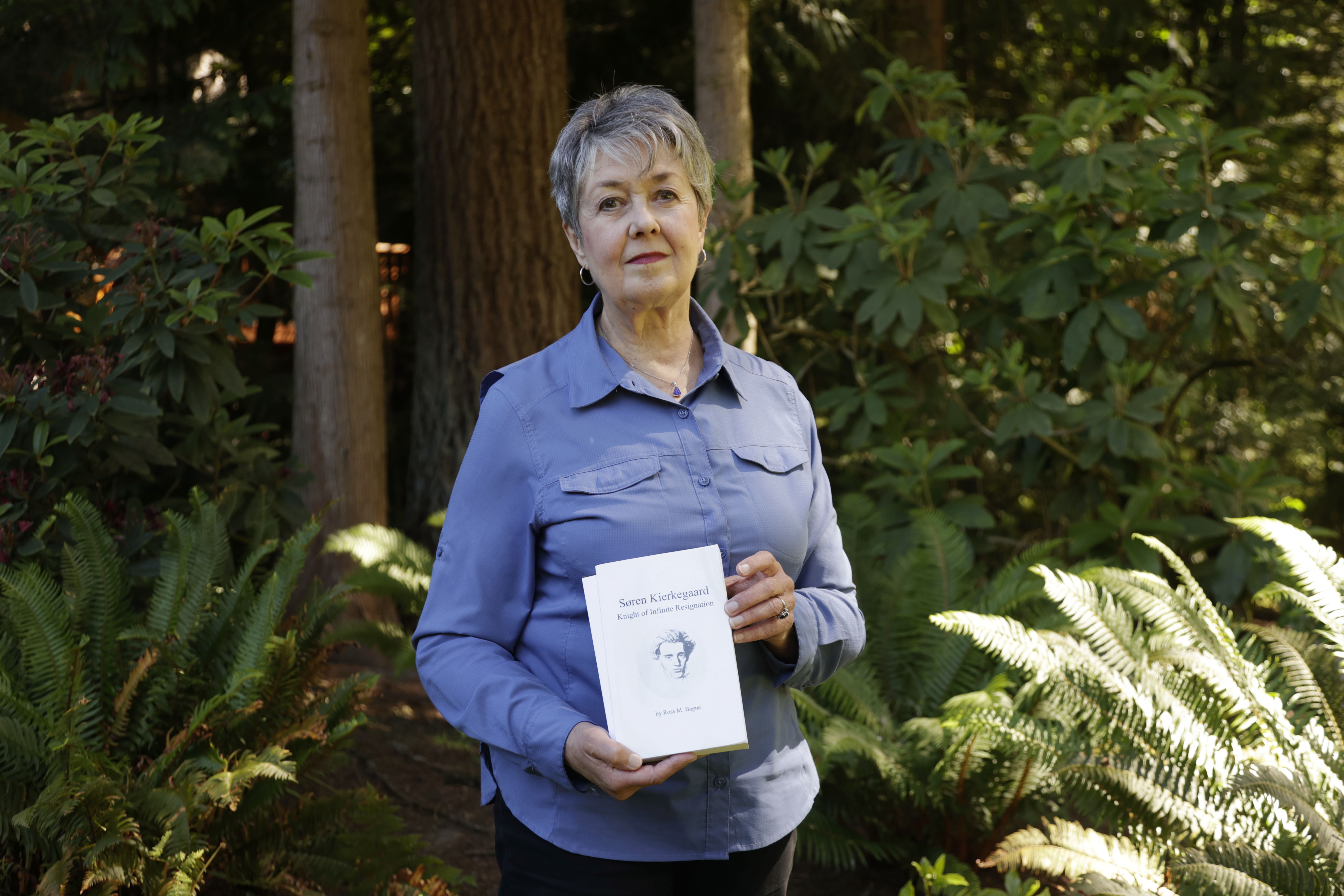 Karen McKnight stands in her backyard on Saturday, June 19, 2021, in Sammamish, Wash., holding two books written by her brother Ross Bagne of Cheyenne, Wyo. Nearly all COVID-19 deaths in the United States now are in people who weren’t vaccinated like Bagne, a staggering demonstration of how effective the vaccines have been
