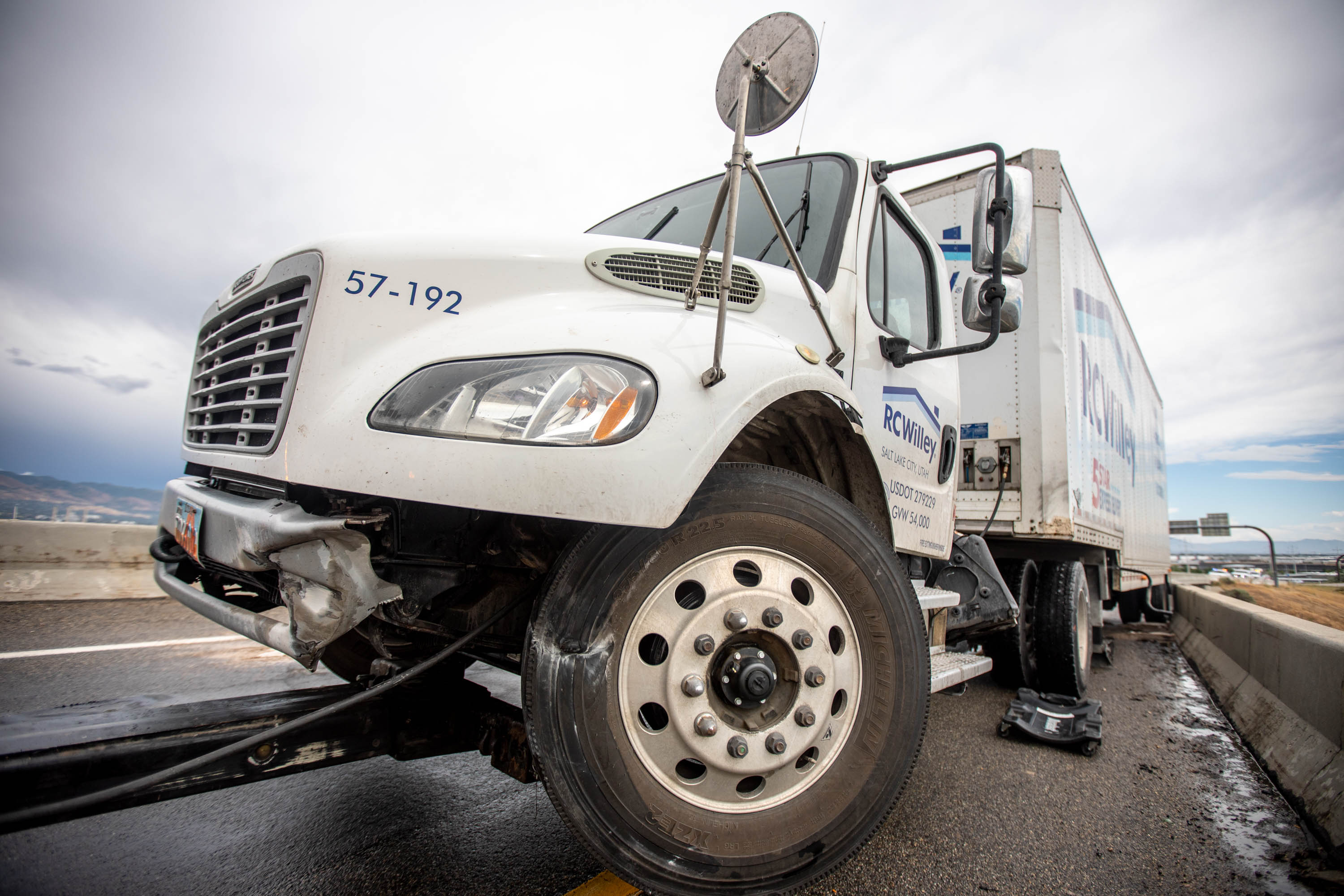 An RC Willey truck that collided with the median on I-215 west near I-80 is pictured in Salt Lake City on Thursday, June 24, 2021. According to Utah Highway Patrol officials, the truck was traveling northbound on I-215 west when it veered to the left, striking and then going over, and onto, the concrete barrier. The semi slid along the top of the concrete barrier for about 50 yards before coming to rest. The tractor of the semi was hanging over the edge of the structure, approximately 50 feet above traffic.