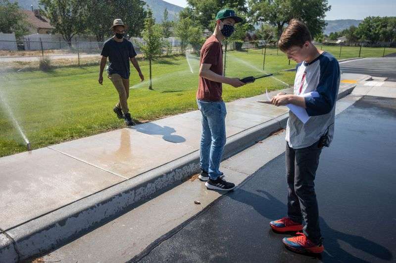 Interns Isaac Middlemas, left, Jaron Tsao and Asher Stewart check sprinklers for their type and if they can be more efficient at Altara Elementary School in Sandy on June 17, 2021.