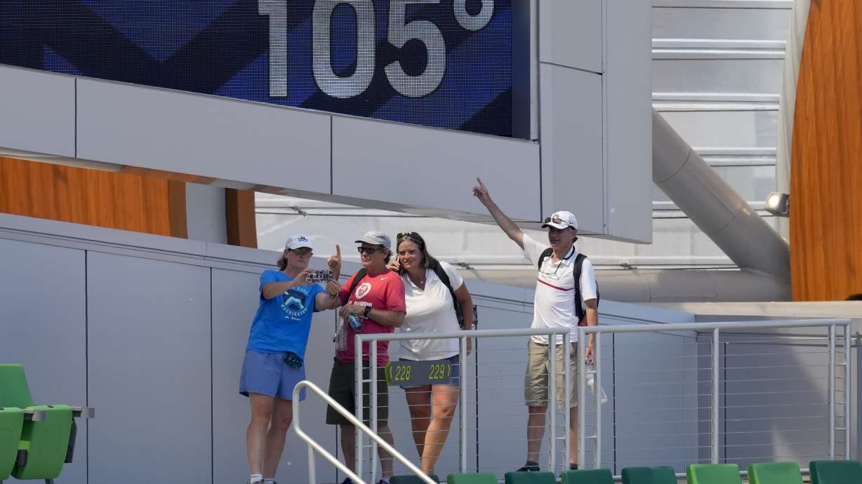 Fans pose for a picture near a sign displaying the current temperature at the U.S. Olympic Track and Field Trials Sunday, June 27, 2021, in Eugene, Ore. Events were postponed until later in the day due to high heat on the trials' final day of competition.