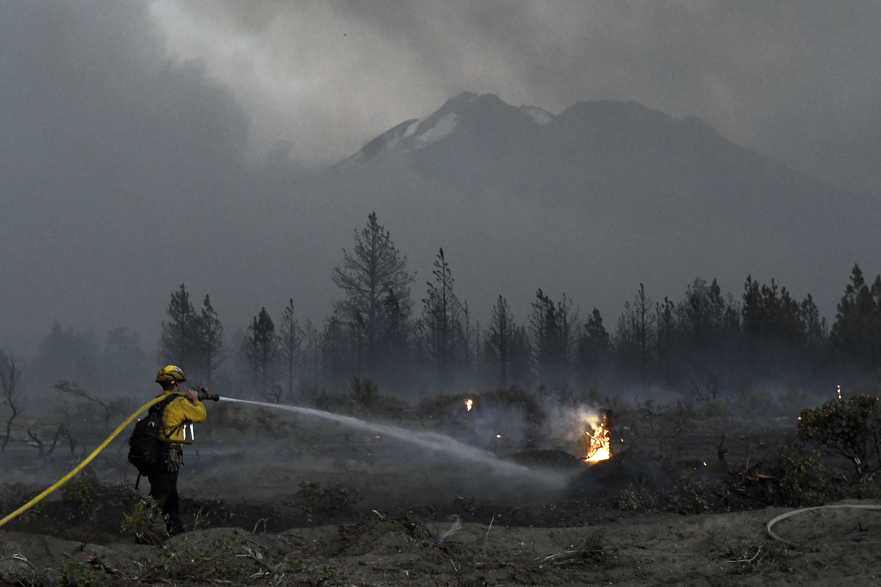 With Mount Shasta in the background, a firefighter cools down hot spots on Monday, June 28, 2021, after the Lava Fire swept through the area north of Weed, Calif. President Joe Biden is set to temporarily raise pay for federal firefighters Wednesday, June 30, 2021.