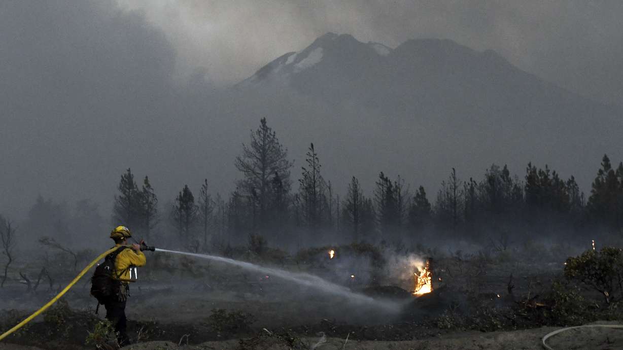 With Mount Shasta in the background, a firefighter cools down hot spots on Monday, June 28, 2021, after the Lava Fire swept through the area north of Weed, Calif. President Joe Biden is set to temporarily raise pay for federal firefighters Wednesday, June 30, 2021.