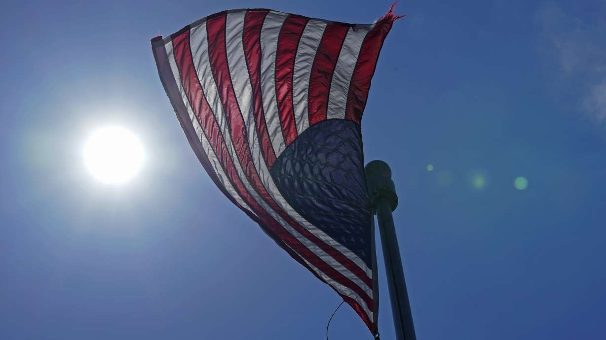 In this Wednesday, June 30, 2021 photo, a U.S. flag flies with the sun in the background in downtown Seattle. As outlandish as the killer heat wave that struck the Pacific Northwest and other areas was, it fit into a decades-long pattern of uneven summer warming in the United States, climate scientists say and federal weather records show.