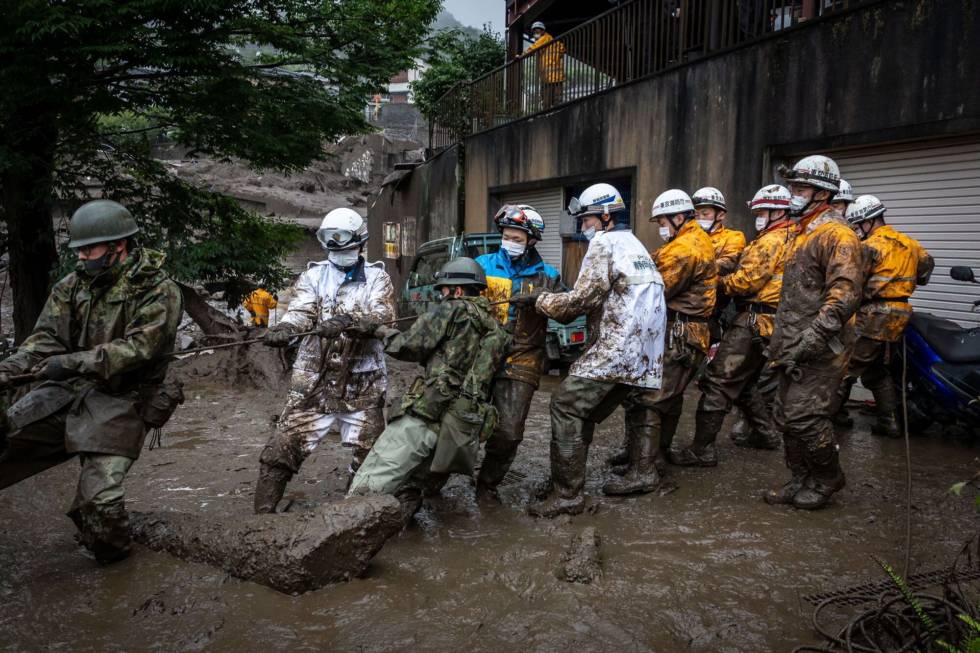 Rescue workers pull a rope to remove debris from a house damaged by a landslide on Sunday July 4, 2021 in Atami, Shizuoka, Japan. A rescue operation is underway after a landslide, caused by torrential rain, tore through the Japanese resort city of Atami, killing two and leaving around twenty missing.