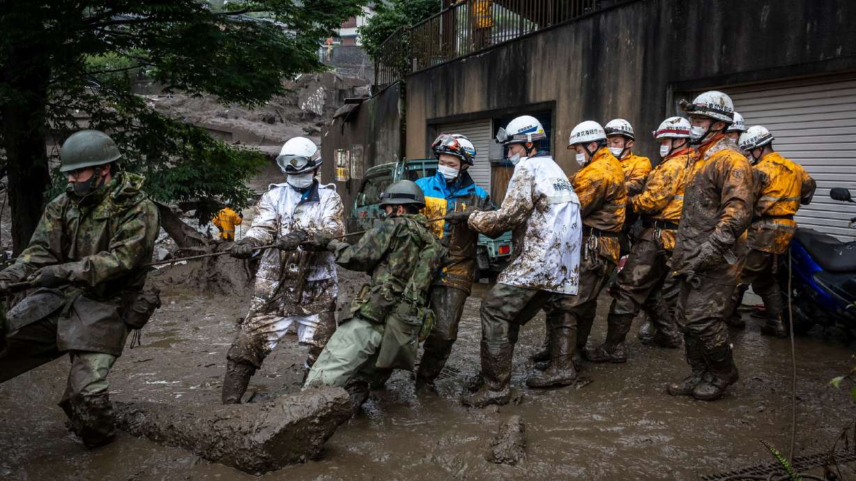 Rescue workers pull a rope to remove debris from a house damaged by a landslide on Sunday July 4, 2021 in Atami, Shizuoka, Japan. A rescue operation is underway after a landslide, caused by torrential rain, tore through the Japanese resort city of Atami, killing two and leaving around twenty missing.
