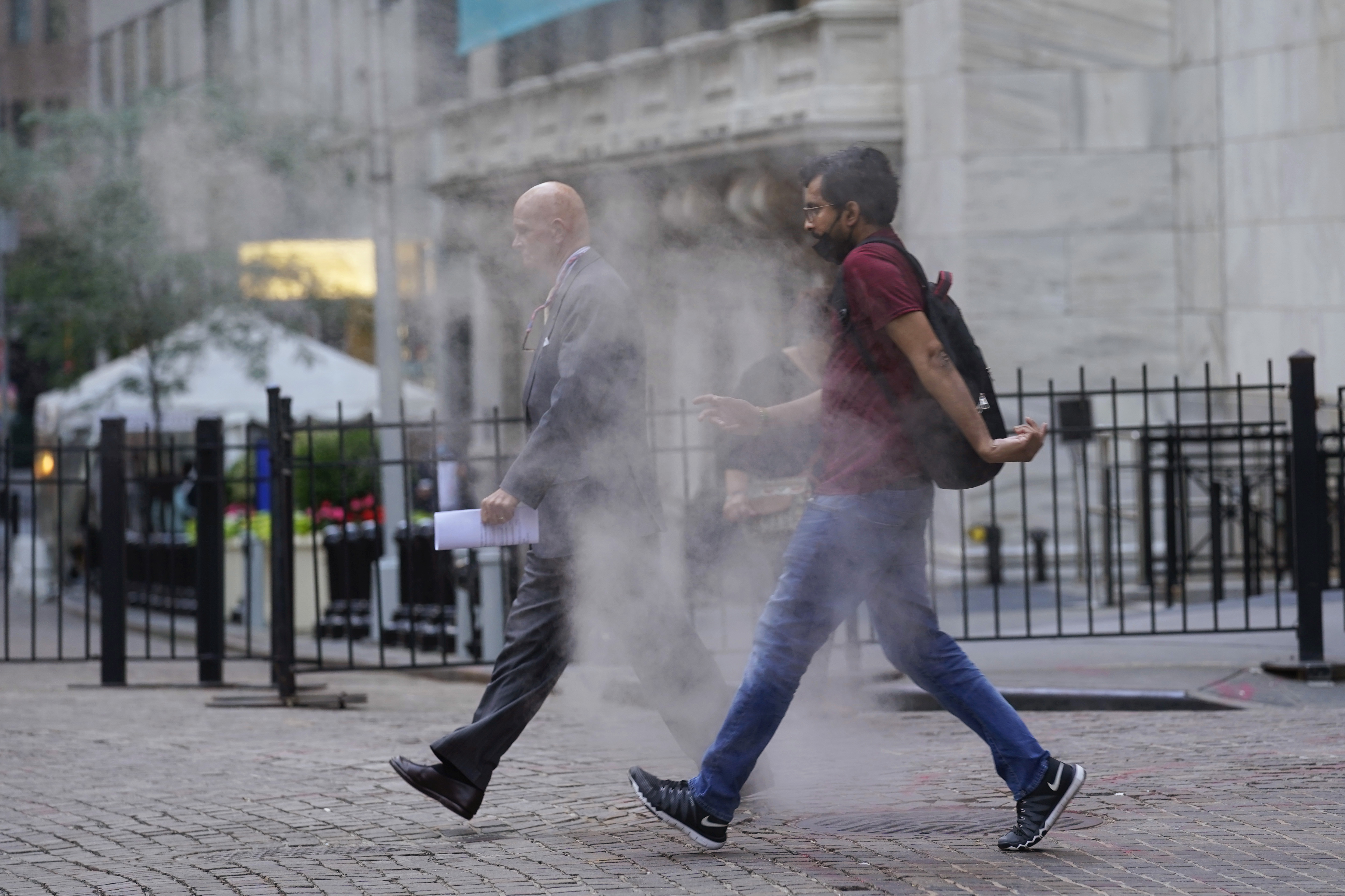 In this June 16, 2021 file photo, people walk through steam from a street grating during the morning commute in New York.   Companies around the U.S. are scrambling to figure out how to bring employees back to the office after more than a year of them working remotely. Most are proceeding cautiously, trying to navigate declining COVID-19 infections against a potential backlash by workers who are not ready to return. 