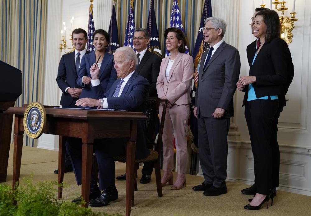 President Joe Biden hands out a pen after signing an executive order aimed at promoting competition in the economy, in the State Dining Room of the White House, Friday, July 9, 2021, in Washington. Standing from left, Transportation Secretary Pete Buttigieg, Lina Khan, Chair of the Federal Trade Commission, Health and Human Services Secretary Xavier Becerra, Commerce Secretary Gina Raimondo, Attorney General Merrick Garland, National Economic Council director Brian Deese, obscured, and Jessica Rosenworcel, Acting Chairwoman of the Federal Communications Commission. 
