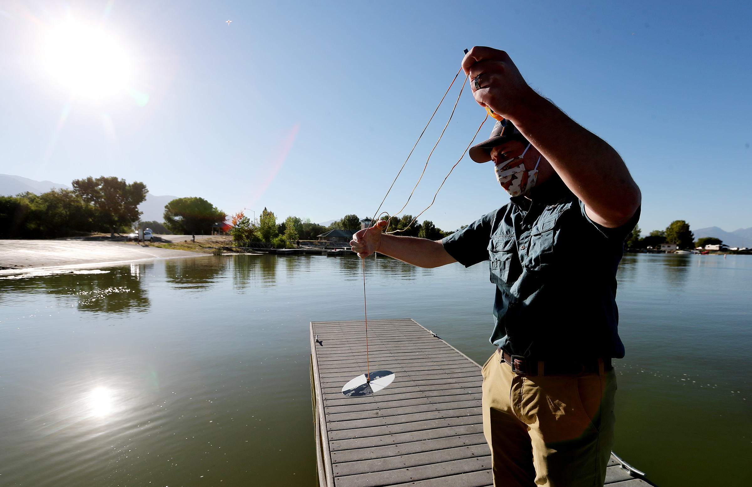 Ryan Van Goethem of SePro demonstrates the use of a Secchi disk to measure the water clarity as the company works to treat an algal bloom at Utah Lake on Friday, Sept. 4, 2020.