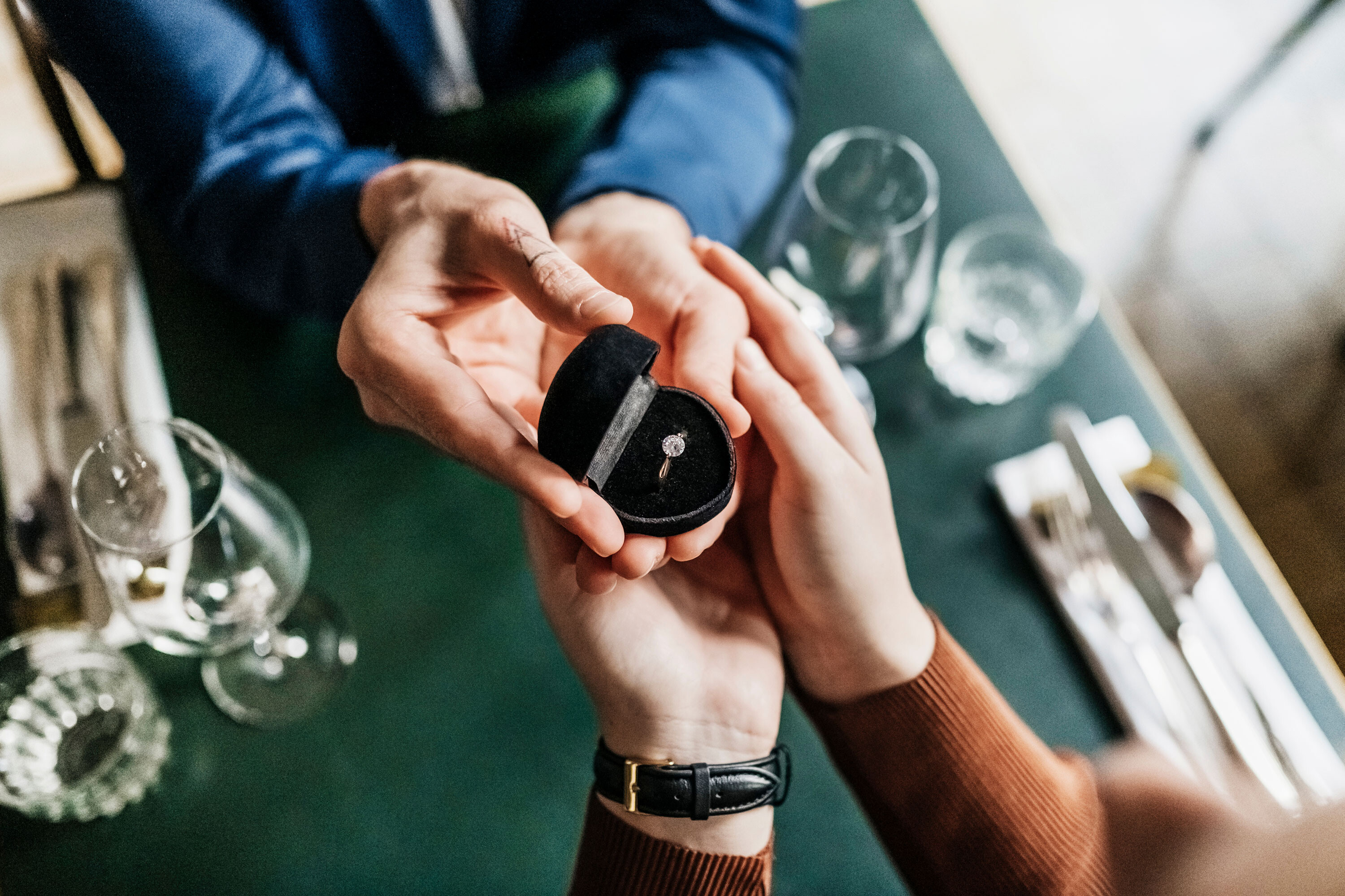 There has been a resurgence in both engagement ring and wedding band sales as couples start returning to normal life following the pandemic. A man is shown presenting his girlfriend with an engagement ring while sitting at a table in a restaurant together.