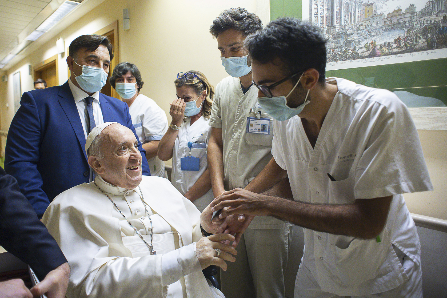 Pope Francis is greeted by hospital staff as he sits in a wheelchair inside the Agostino Gemelli Polyclinic in Rome, Sunday, July 11, 2021, where he was hospitalized for intestine surgery. 