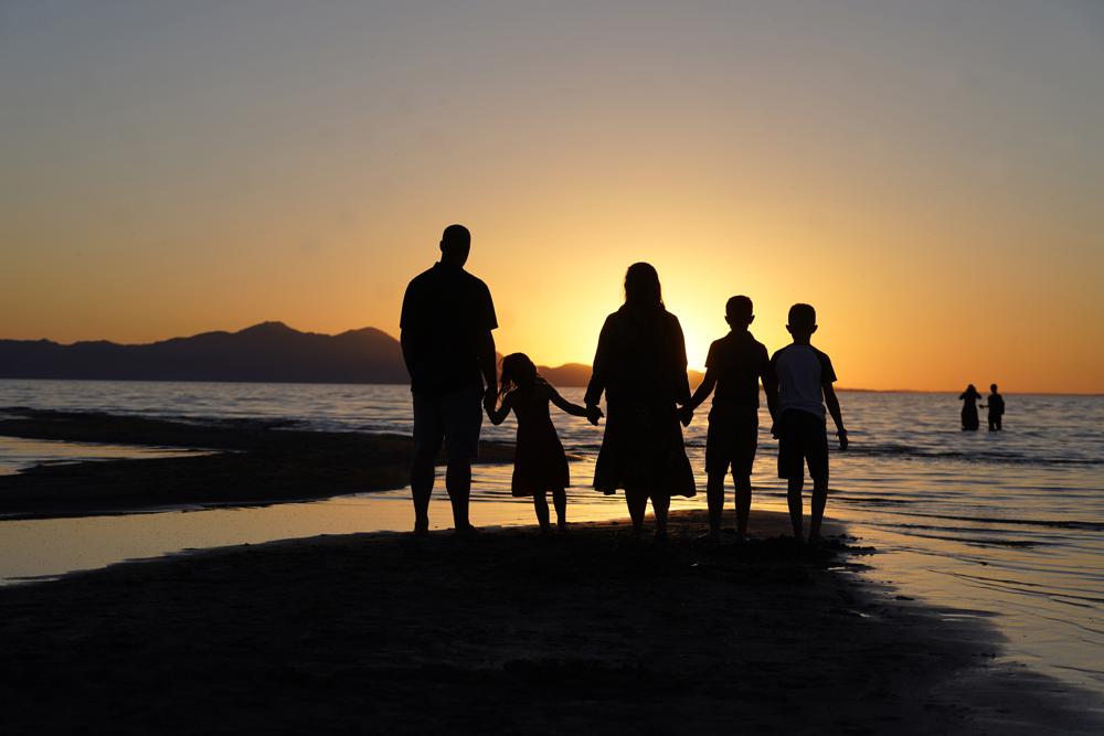 In this June 13, 2021 file photo, people hold hands as they gather at the receding edge of the Great Salt Lake to watch the sunset near Salt Lake City. The lake has been shrinking for years, and a drought gripping the American West could make this year the worst yet.