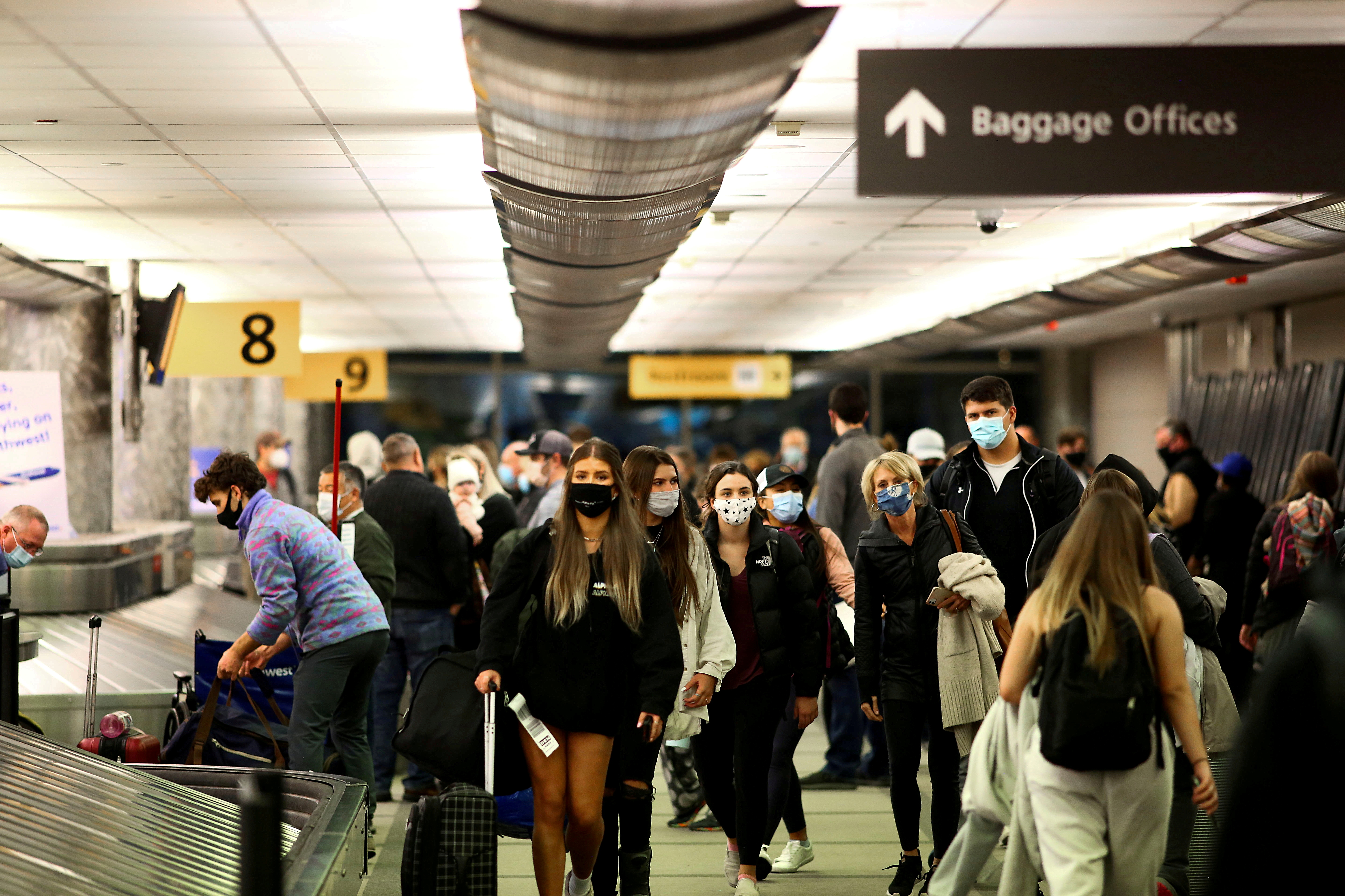 Travelers wearing protective face masks to prevent the spread of the coronavirus disease reclaim their luggage at the airport in Denver, Colorado, Nov. 24, 2020. A White House official says the United States will not lift any existing travel restrictions "at this point" due to concerns over the highly transmissible delta variant and the rising number of U.S. coronavirus cases.