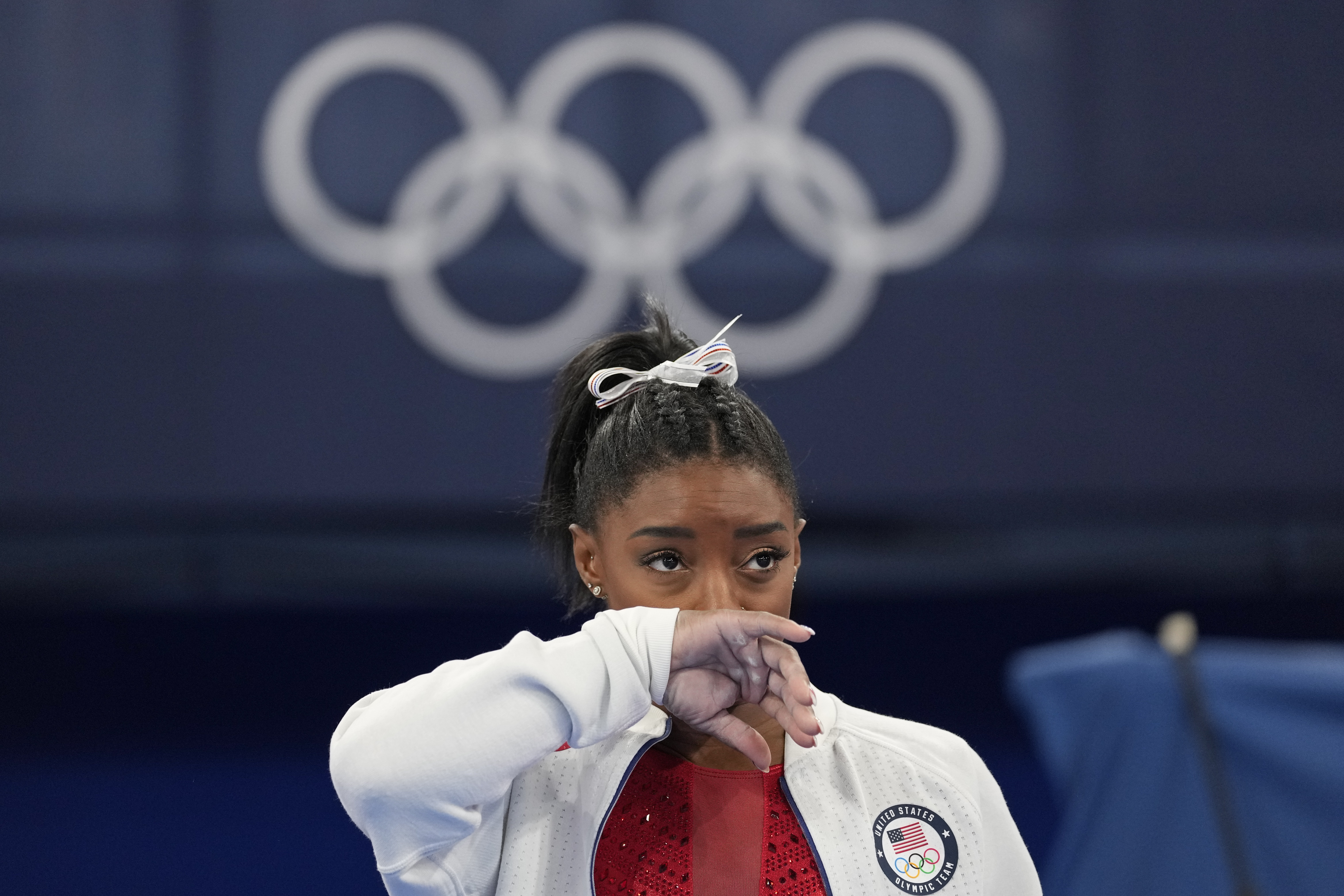 Simone Biles, of the United States, watches gymnasts perform after she exited the team final with an apparent injury, at the 2020 Summer Olympics, Tuesday in Tokyo. Biles huddled with a trainer after landing her vault. She then exited the competition floor with the team doctor.