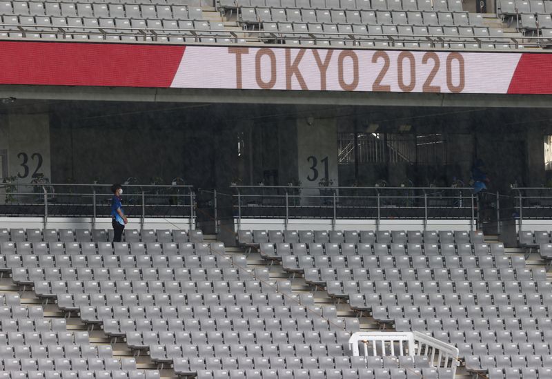Tokyo 2020 Olympics - Rugby Sevens - Women - Pool A - New Zealand v Russian Olympic Committee - Tokyo Stadium - Tokyo, Japan - July 30, 2021. A volunteer wearing a protective face mask takes shelter as he waits for the rain to stop.