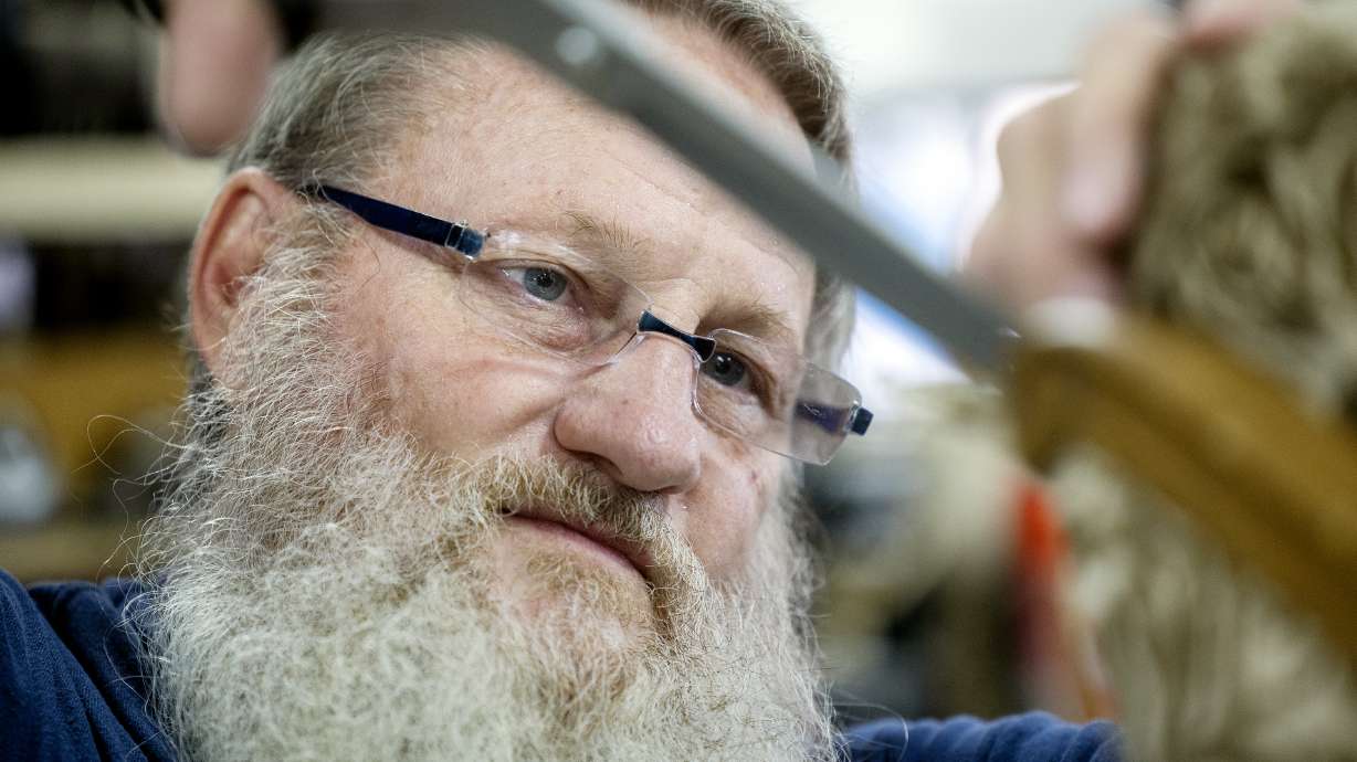 Ken Curtis of KenTeck Custom Upholstery uses a pair of large scissors to trim some of the fabric away as he works on a chair in his West Jordan shop on Friday.