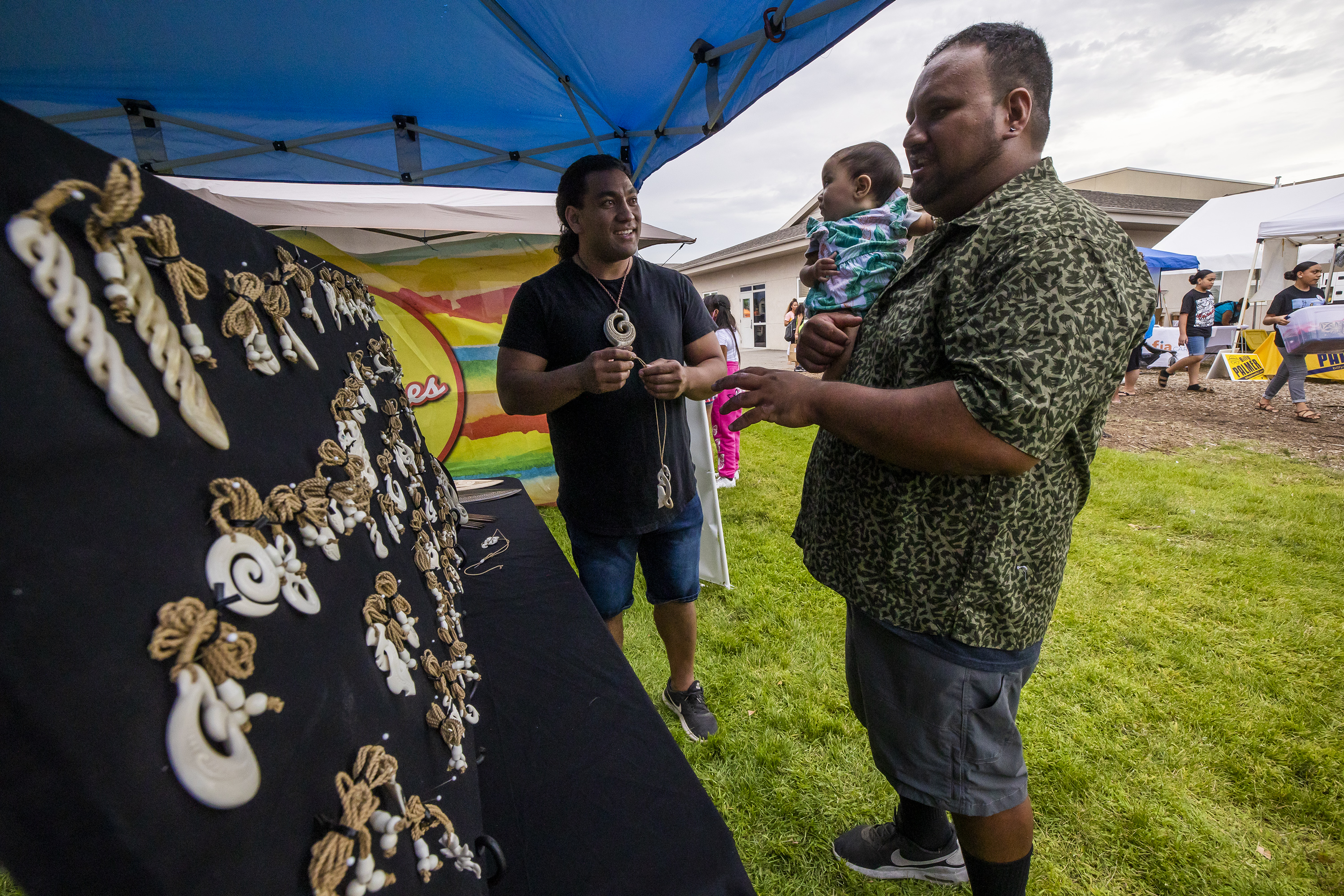 Artist Tane Falevai of Tane Designs, talks with Kale Kamalamalama while he holds his daughter Iolana, as Polynesian Month kicks off at the Pacific Heritage Academy in Salt Lake City on Saturday.