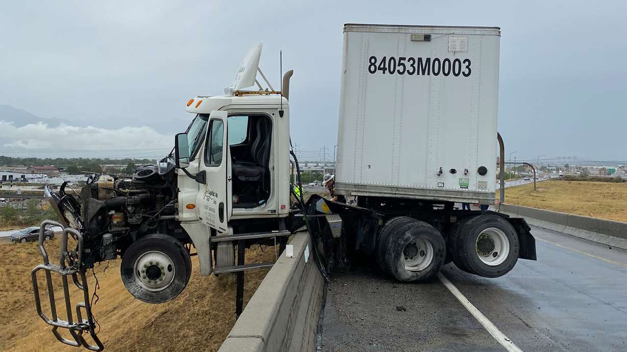 A truck driver was not injured after a Salt Lake City crash left his cab precariously perched on the edge of an I-215 overpass on Monday.