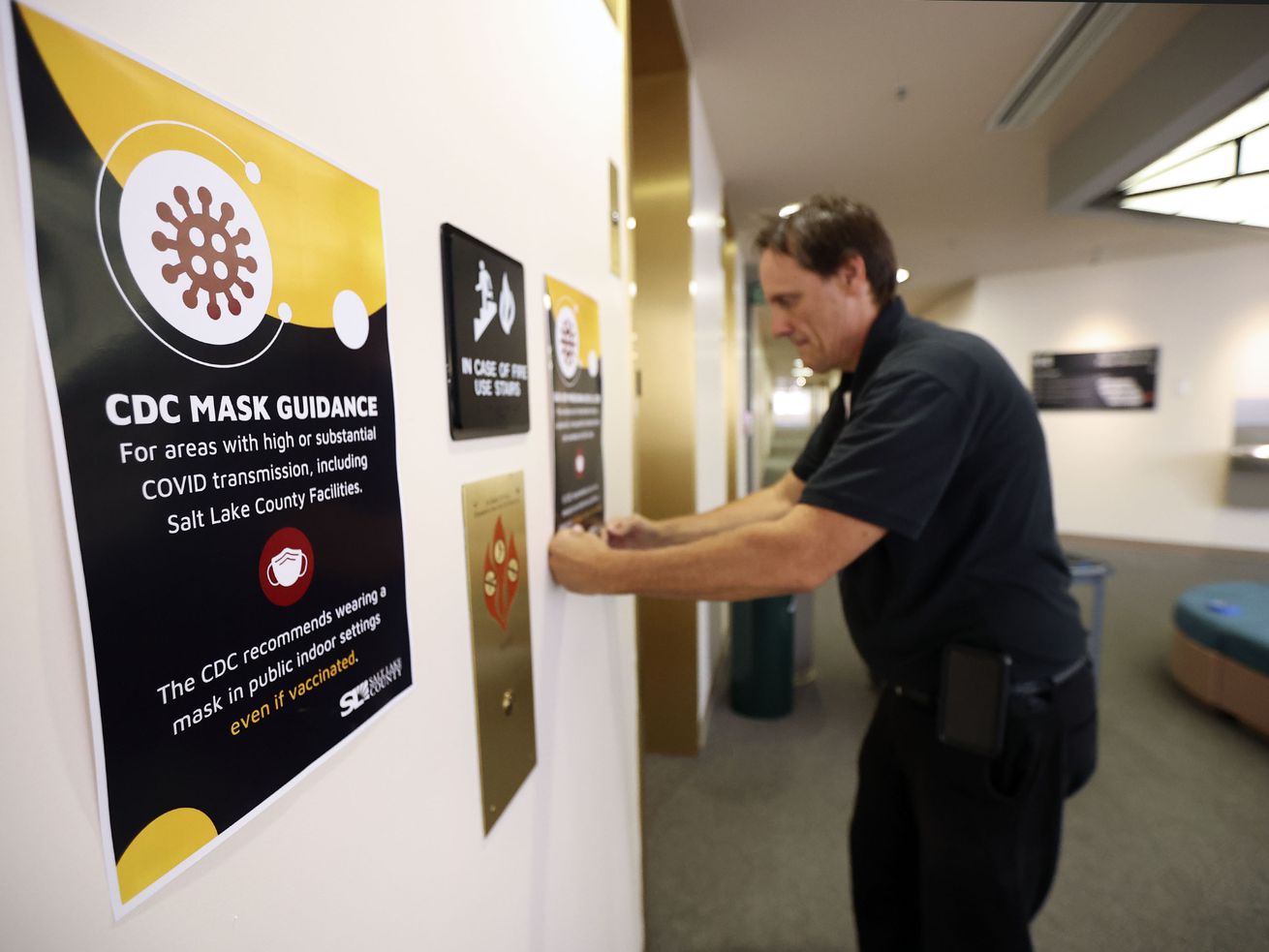 Jeff Buckner, Salt Lake County facilities maintenance supervisor, puts up new signs in the Salt Lake County Government
Center in Salt Lake City reflecting the Centers for Disease Control and Prevention’s updated guidance on masks on Monday. The CDC now recommends masks for all individuals, regardless of vaccination status, inside public places.
