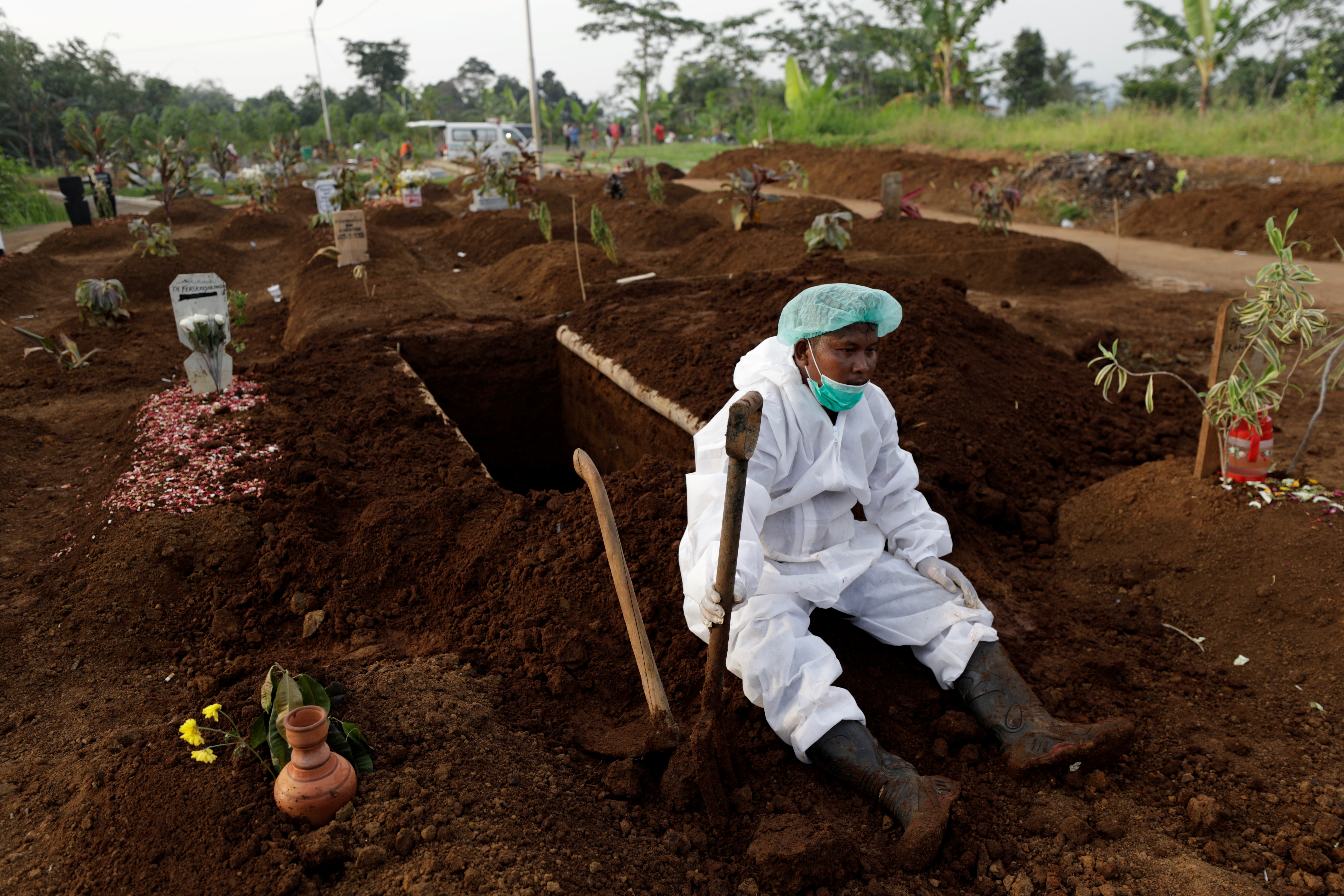 A gravedigger wearing personal protective equipment rests after the burial of 64-year-old Yoyoh Sa'diah who passed away due to complications related to COVID-19 whilst isolating at her home in Bogor, West Java province, Indonesia, July 8, 2021.