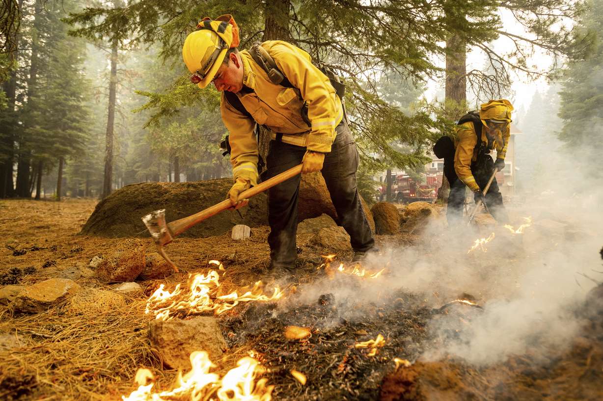 Northern Sonoma County Fire District firefighters Erik Padilla, left, and Joe Young extinguish hot spots while protecting Lake Almanor West homes from the Dixie Fire Thursday, in Plumas County, Calif. They work out of the Geyserville Fire Station.