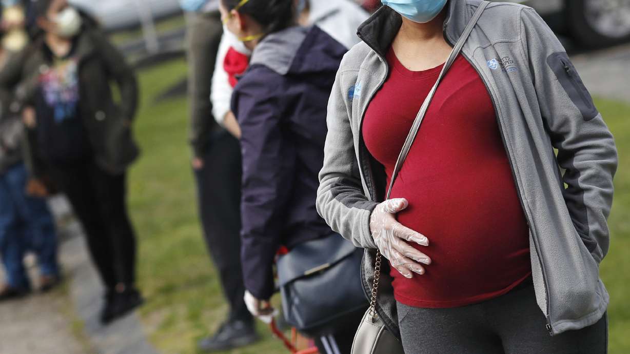 A pregnant woman wearing a face mask and gloves holds her belly as she waits in line for groceries at St. Mary's Church in Waltham, Mass. The Centers for Disease Control and Prevention urged all pregnant women Wednesday to get the COVID-19 vaccine as hospitals in hot spots around the U.S. see disturbingly high numbers of unvaccinated mothers-to-be seriously ill with the virus.