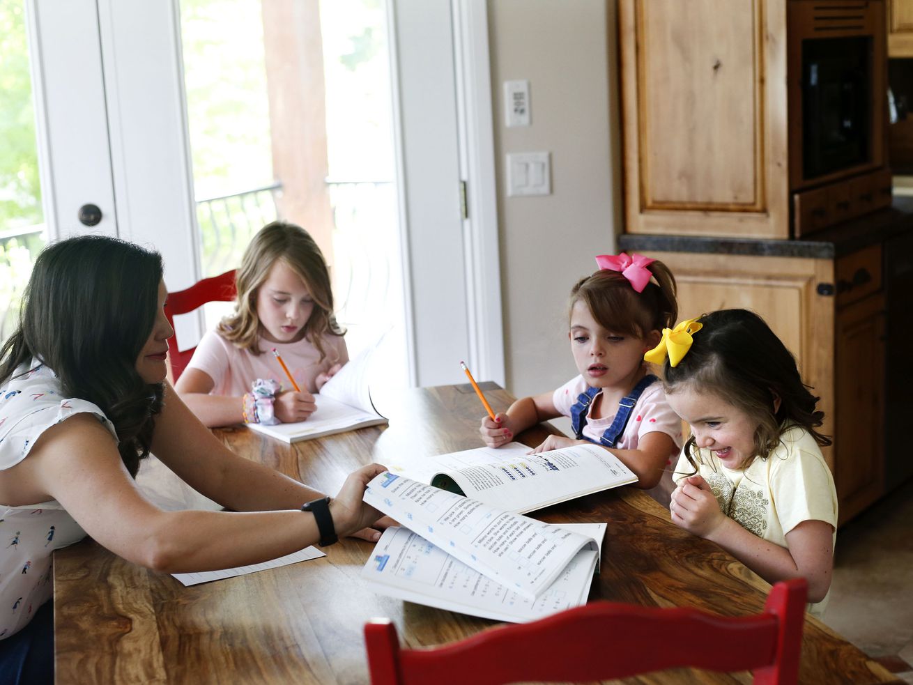 Vivian Seger, 6, right, gets excited about getting a peek at her new math book with her sisters Gwendolyn, 6, Lydia, 10, and her mother, Melissa, at their South Jordan home on Friday. Seger and her husband, Rob, will home-school their children this year, a decision solidified after the Salt Lake County Council voted 6-3 along party lines Thursday to terminate a health order that would have required all children under age 12 to wear masks in school.