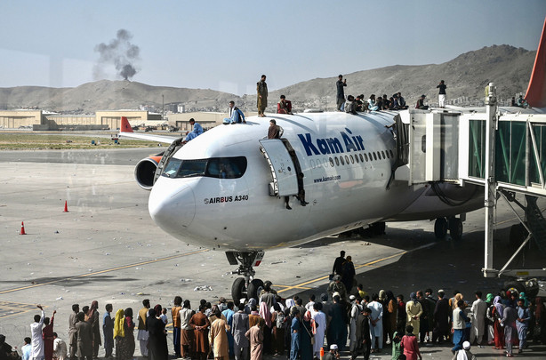 Afghan people climb atop a plane as they wait at the Kabul airport on Aug. 16. The chaotic end to America's longest war has sparked the biggest crisis of President Joe Biden's seven months in the White House: questions about who, if anyone, would be held responsible.