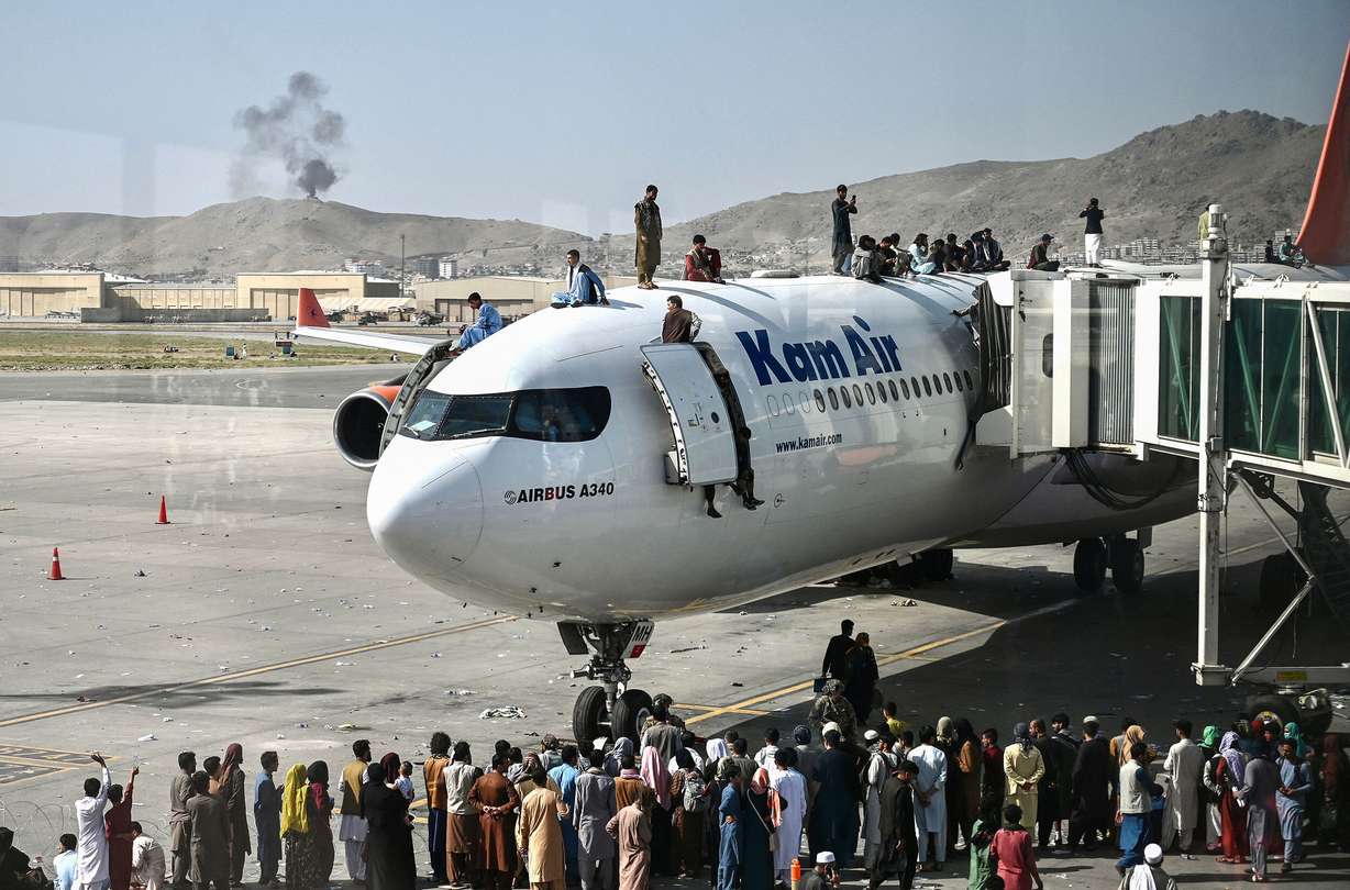 Afghan people climb atop a plane as they wait at the Kabul airport on Aug. 16. The chaotic end to America's longest war has sparked the biggest crisis of President Joe Biden's seven months in the White House: questions about who, if anyone, would be held responsible.