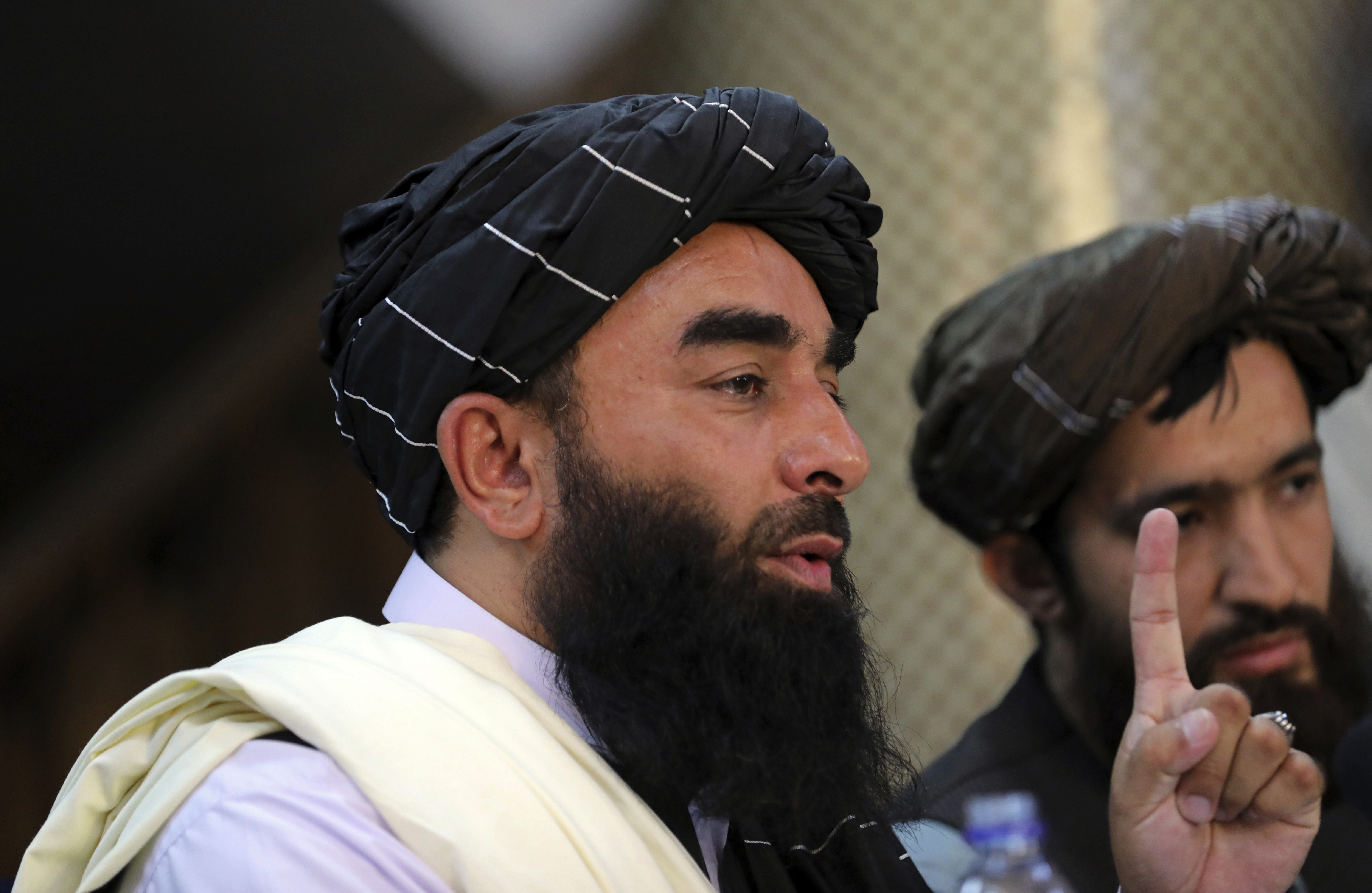 Taliban spokesman Zabihullah Mujahid, left, speaks at his first news conference at the Government Media Information Center, in Kabul, Afghanistan, Tuesday. The Taliban have agreed to allow "safe passage" from Afghanistan for civilians struggling to join a U.S.-directed airlift from the capital.