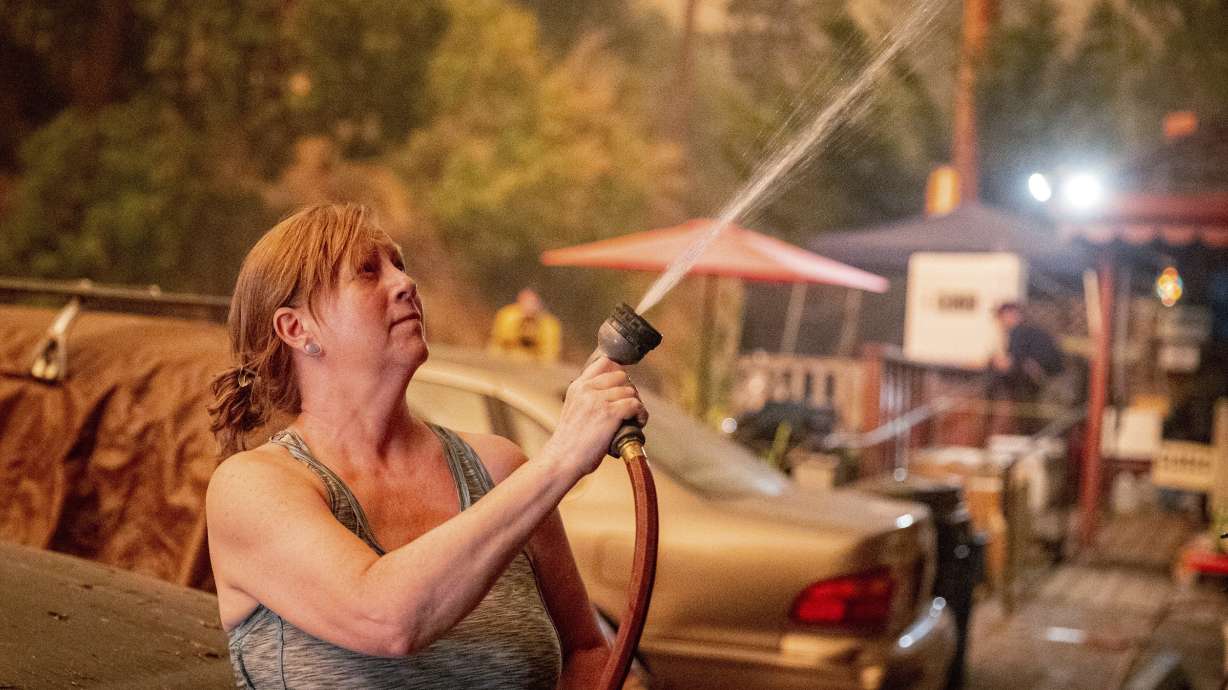 Jennifer Whitmore sprays her home with water as the Caldor fire burns near White Hall, California on Tuesday. Wind-driven wildfires raged Wednesday through drought-stricken forests in the mountains of Northern California after incinerating hundreds of homes and forcing thousands of people to flee to safety.