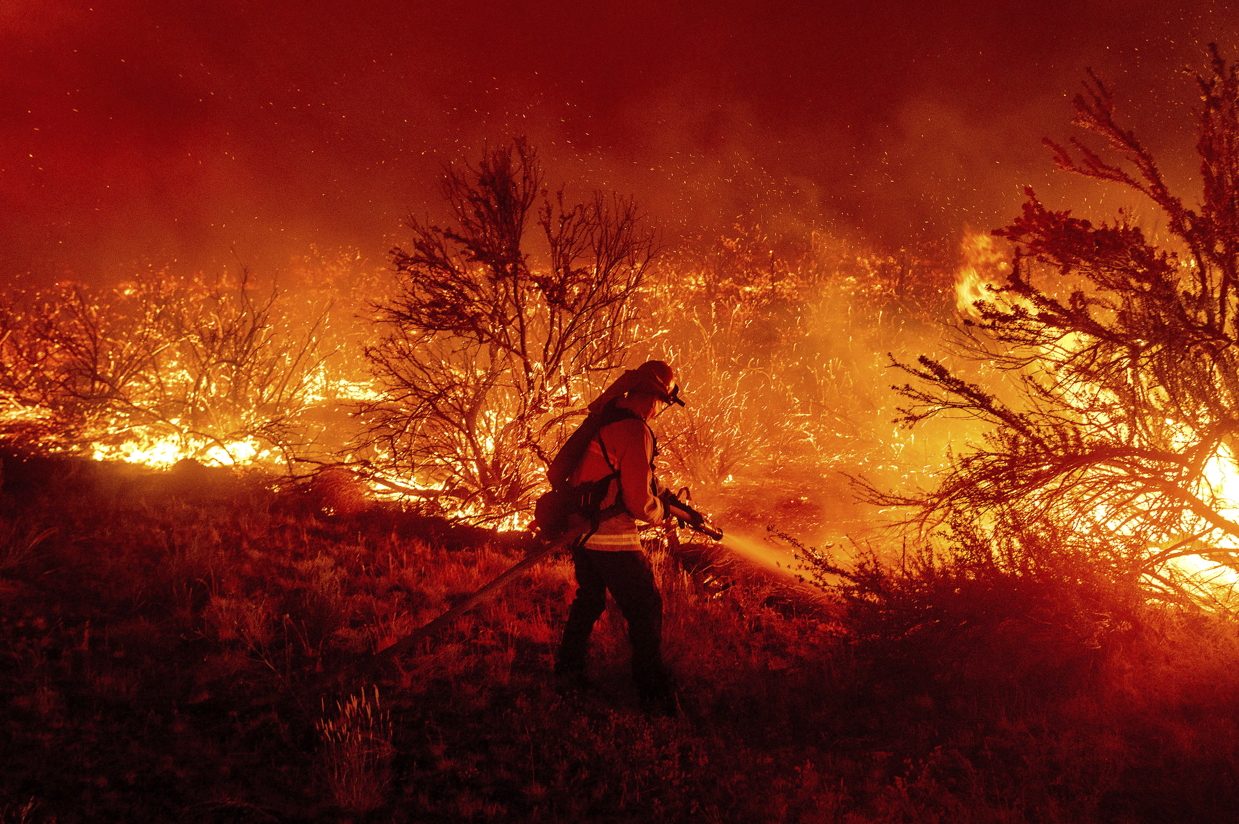 A firefighter battles the Dixie Fire in Lassen County, Calif. Aug. 16. Wildfire managers are often asked why firefighters simply don't put out the flames to save their homes. 