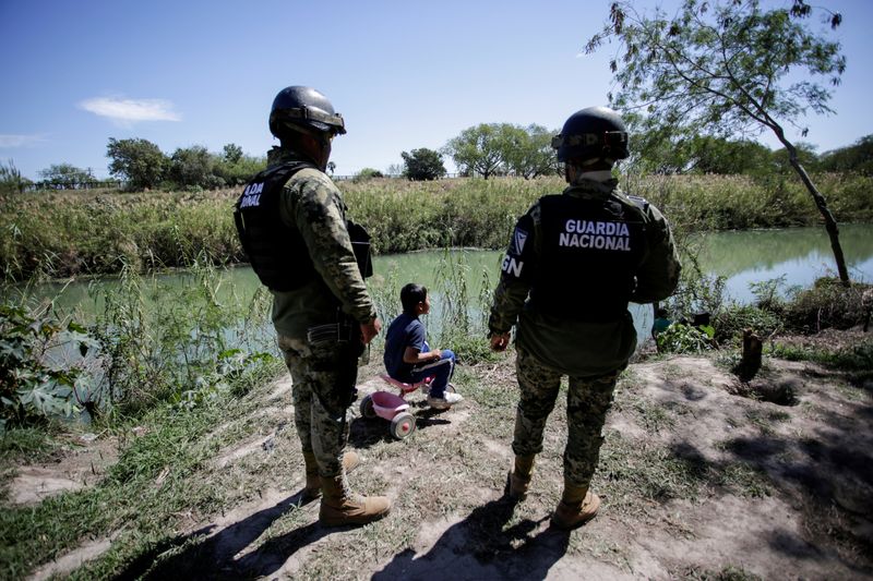 A migrant boy, an asylum seeker sent back to Mexico from the U.S. under the "Remain in Mexico" program is seen near two members of the Mexican National Guard at a provisional campsite near the Rio Bravo in Matamoros, Mexico, on February 27, 2020.
