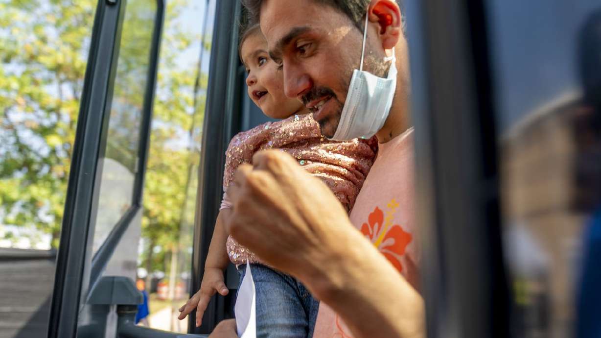 An Afghan man carries a girl as he and other refugees arrive at a processing center in Chantilly, Va., on Monday after arriving on a flight at Dulles International Airport.