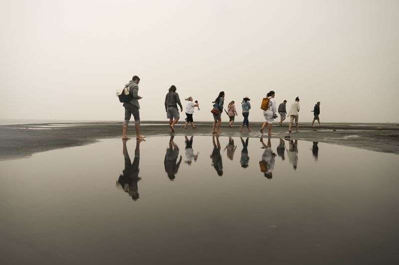 Visitors to Silver Sand Beach at Great Salt Lake Marina
are reflected on still water as they walk around during a rainstorm
on Aug. 18.