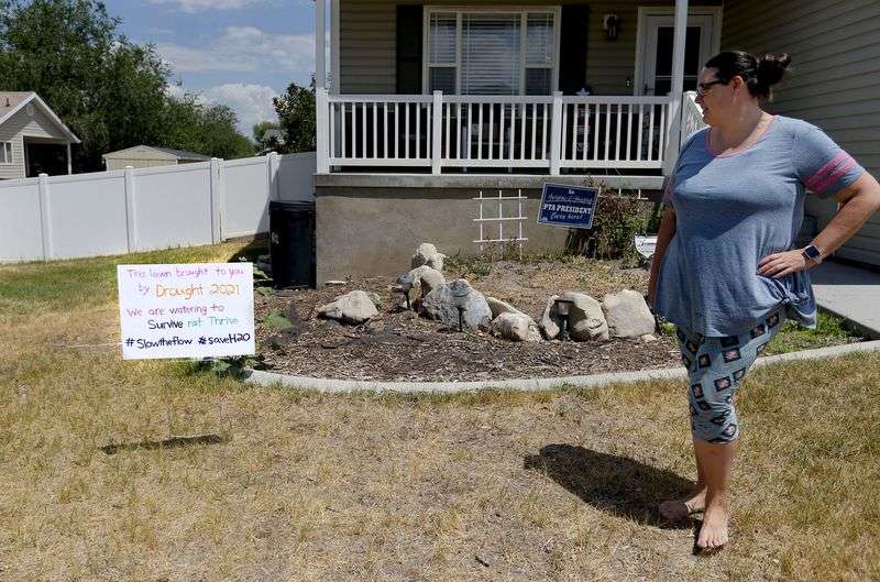 Emmalee Nelson Thompson looks at a sign in her Magna yard that explains her decision not to water her lawn on Friday, July 2, 2021.