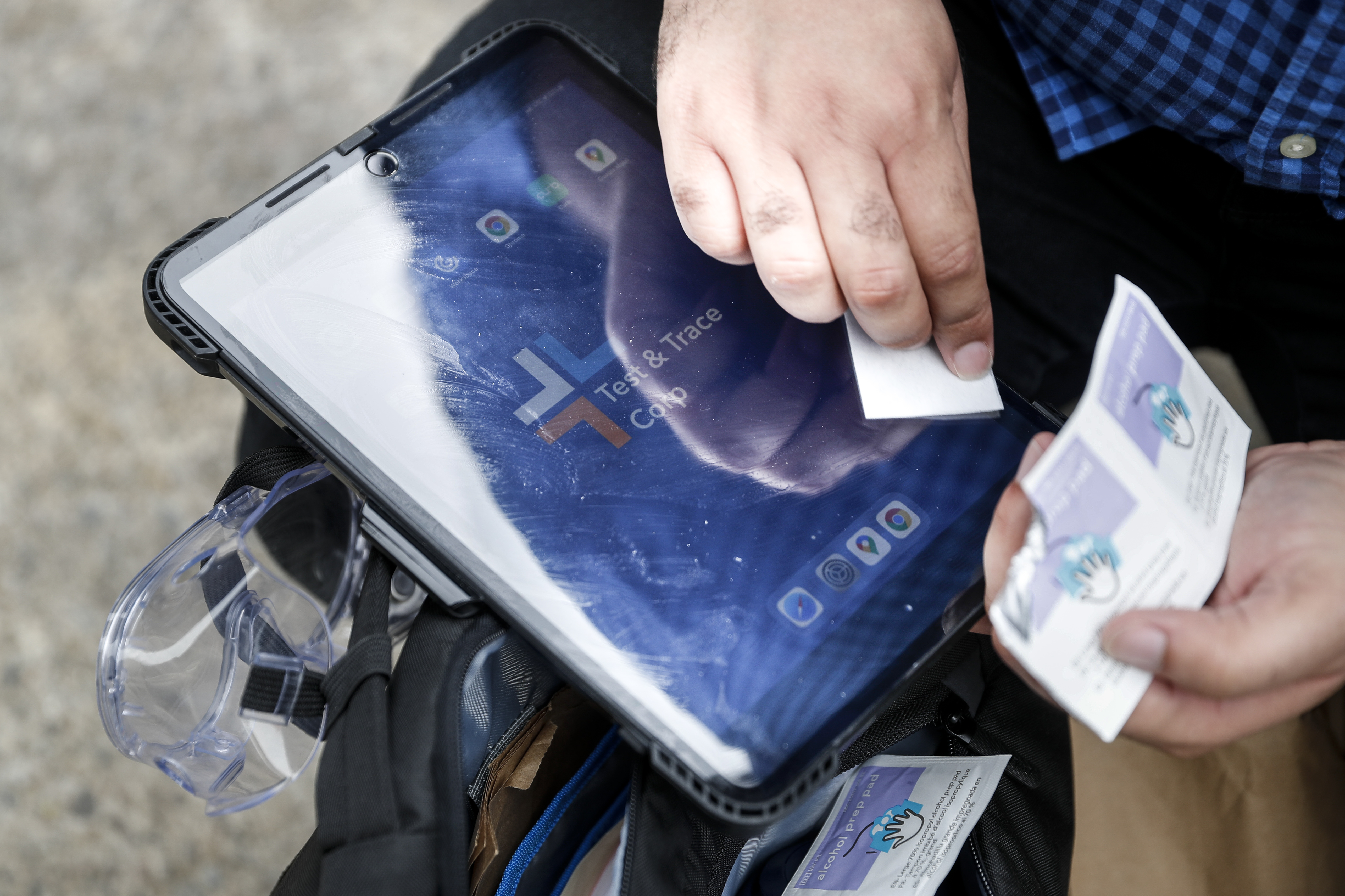 Joseph Ortiz, a contact tracer with New York City's Health + Hospitals, disinfects his tablet after leaving a potential patient's home in New York on Aug. 6, 2020. Health investigators across the U.S. are finding it nearly impossible to keep up with the deluge of new COVID-19 infections.