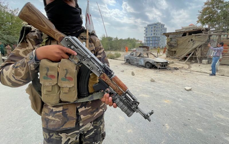 A member of Taliban forces stands guard as Afghan men take pictures of a vehicle from which rockets were fired, in Kabul, Afghanistan, on Monday.