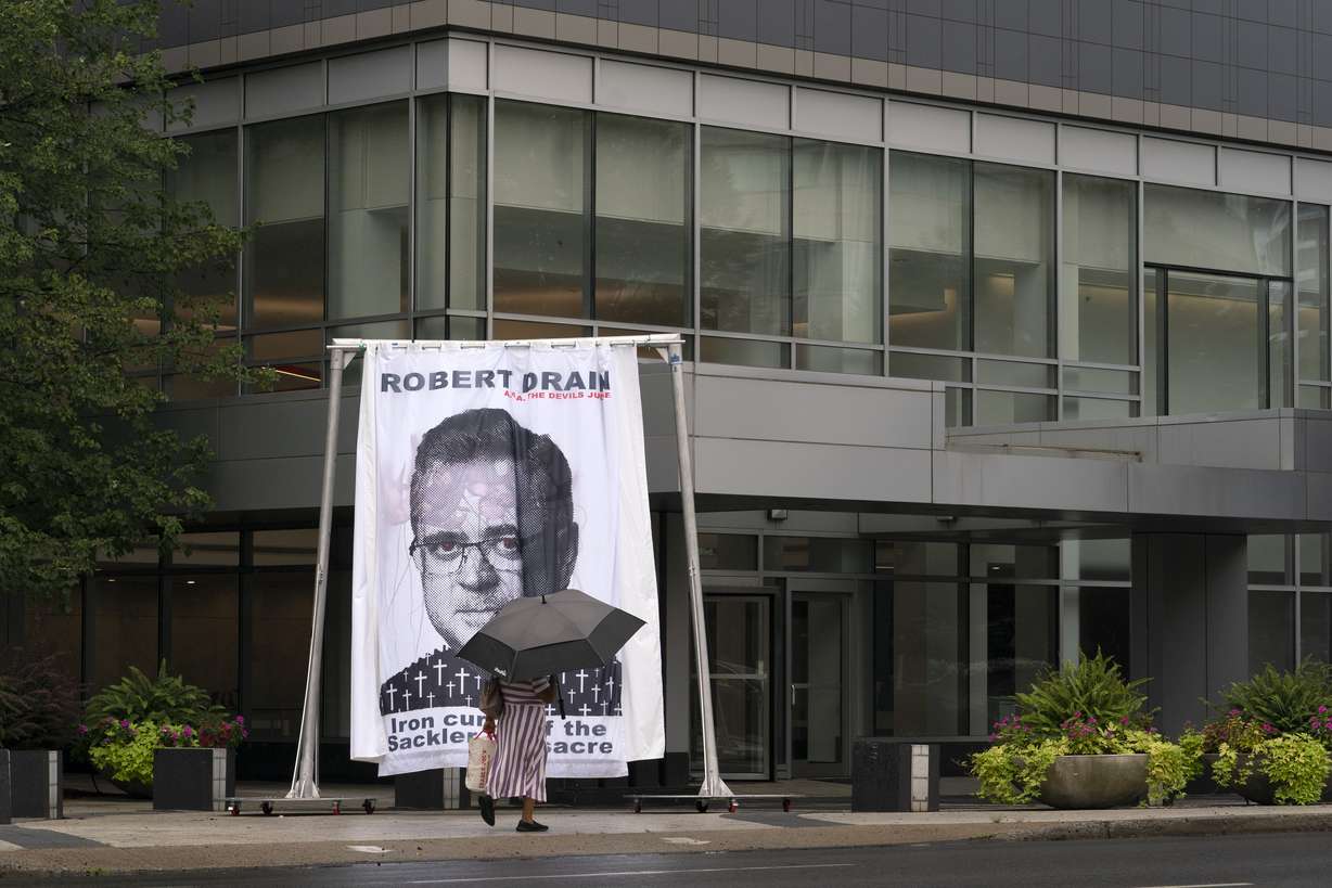 A woman walks by an image of federal bankruptcy judge Robert Drain that was installed by protesters in front of Purdue Pharma's headquarters, Wednesday in Stamford, Conn. The judge is preparing to rule on a plan for OxyContin maker Purdue Pharma to settle lawsuits brought by governments and others over its role in the opioid crisis.