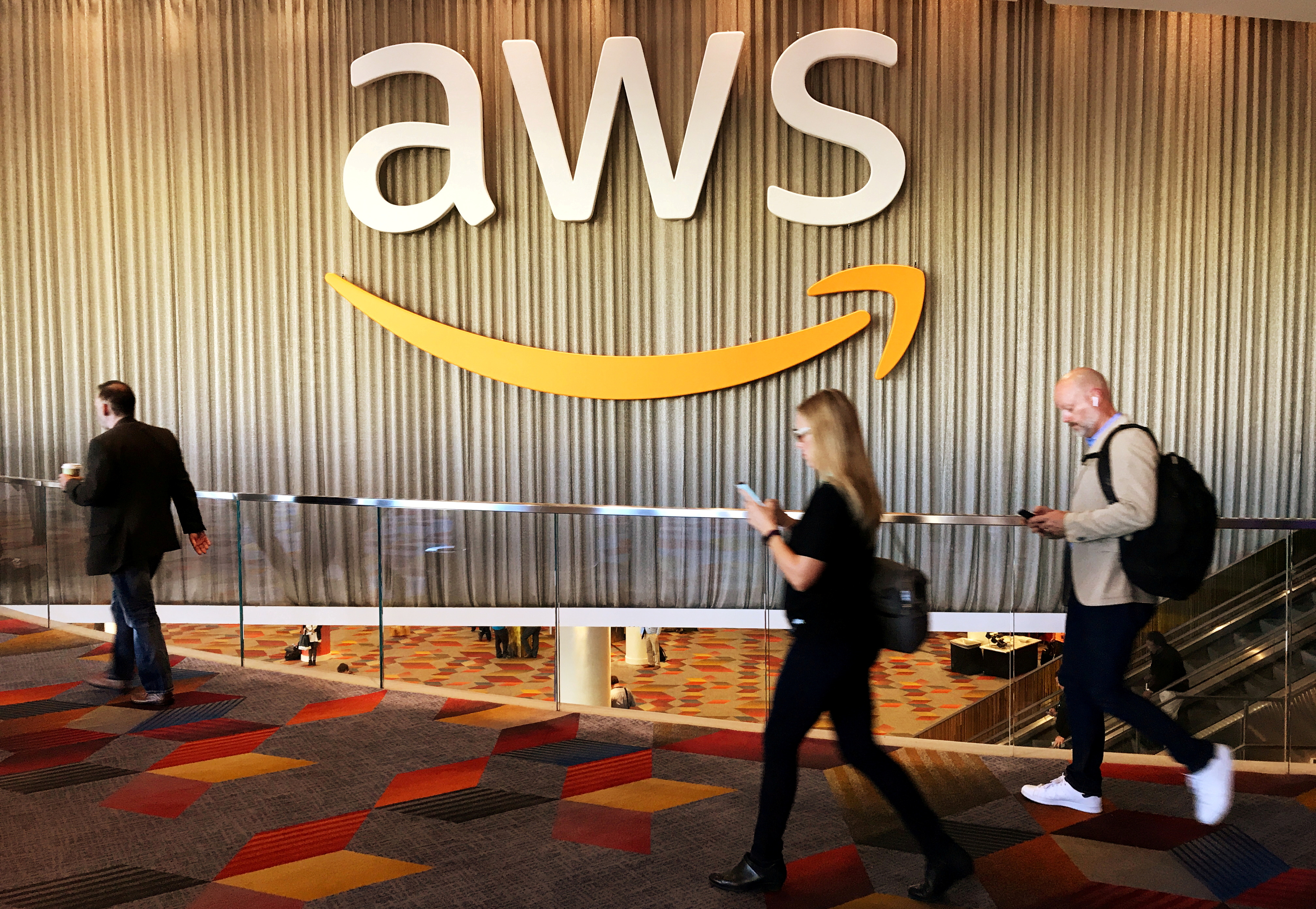 Attendees at Amazon.com annual cloud computing conference walk past the Amazon Web Services logo in Las Vegas, Nevada, U.S., November 30, 2017. Amazon plans to take a more proactive approach to determine what types of content violate its cloud service policies, such as rules against promoting violence, and enforce its removal.