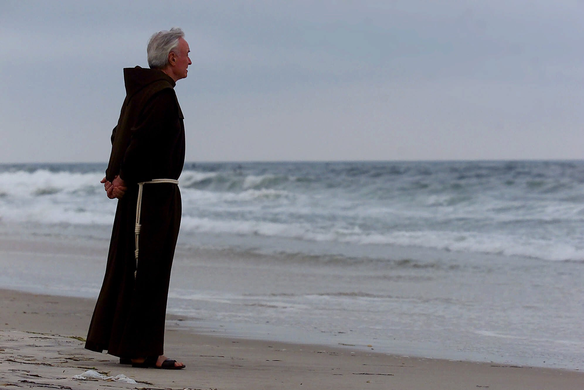 Father Mychal Judge, a chaplain with the New York City Fire Department, stands at the shore before a service where 230 candles were lit for the July 17, 1996, victims of TWA Flight 800, at Smith Point Park in Shirley, N.Y.