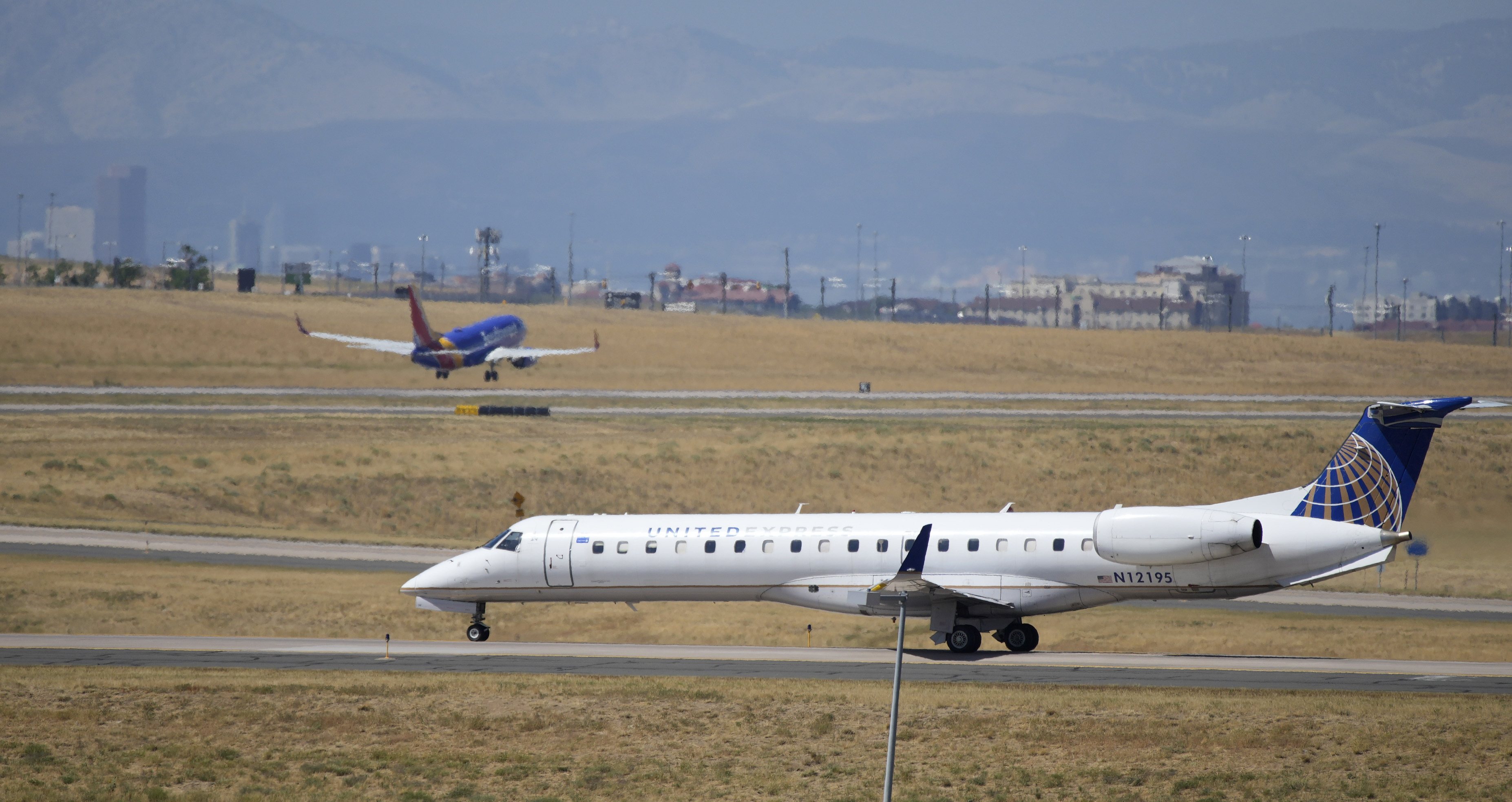 A United Express jet taxis down a runway as a Southwest Airlines plane takes off in the background at Denver International Airport, Tuesday, Aug. 24, in Denver.