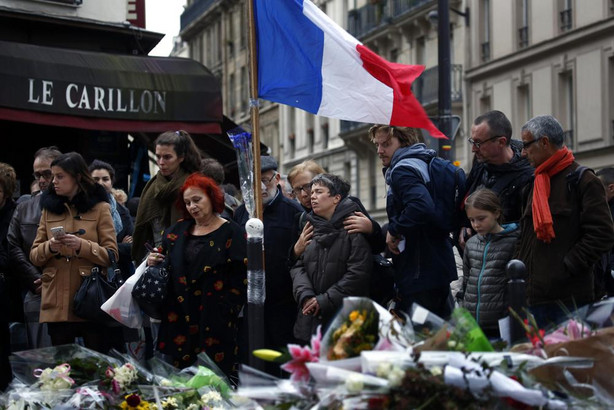 In this Nov. 16, 2015, photo people gather in front of Le Carillon cafe, a site of the recent attacks, in Paris. French President Francois Hollande says the Paris attacks targeted "youth in all its diversity" and that the victims were of 19 different nationalities.