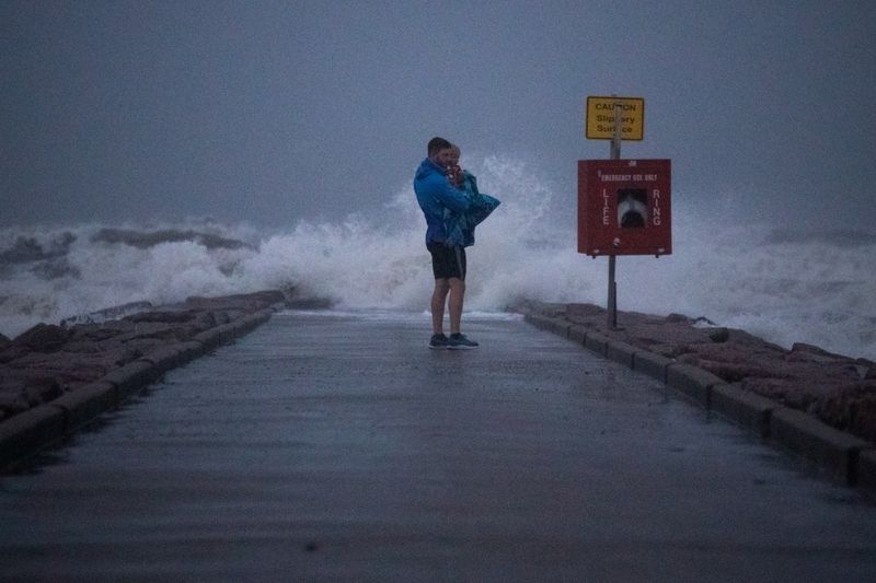 Local resident John Smith holds his 18-month-old son Owen as he stands near breaking waves on a pier ahead of the arrival of Tropical Storm Nicholas in Galveston, Texas, Mondady.