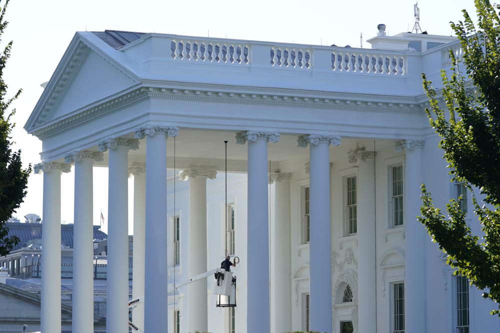A worker works on the light fixture over the North Portico of the White House in Washington, Friday, Sept. 3, 2021. The White House is warning about severe cuts to disaster relief, Medicaid, infrastructure grants, school money and other programs if Congress fails to raise the U.S. debt limit.