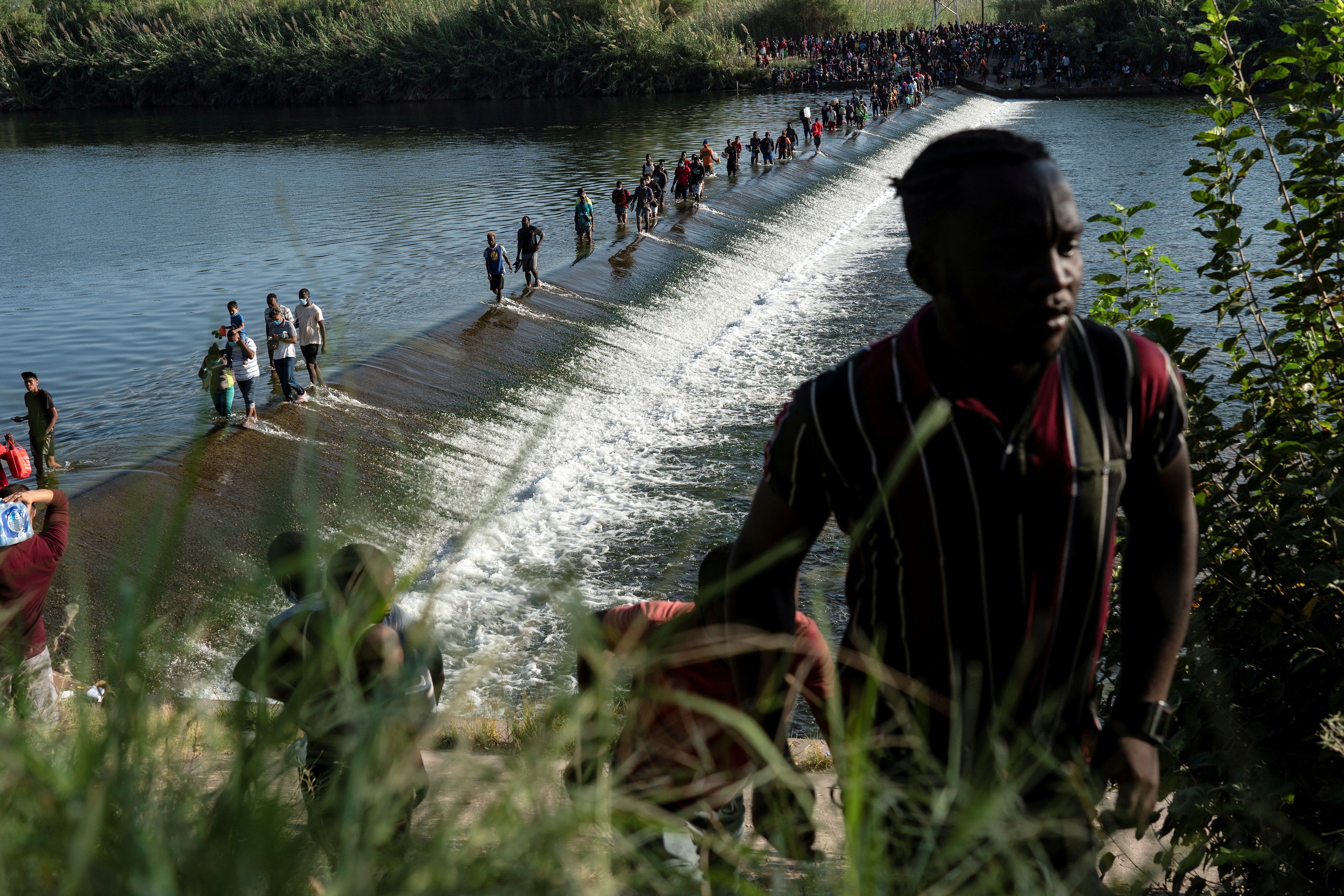 Migrants seeking asylum in the U.S. walk in the Rio Grande river near the International Bridge between Mexico and the U.S., as they wait to be processed, in Ciudad Acuna, Mexico, on Sept. 16. According to officials, some migrants cross back and forth into Mexico to buy food and supplies.
