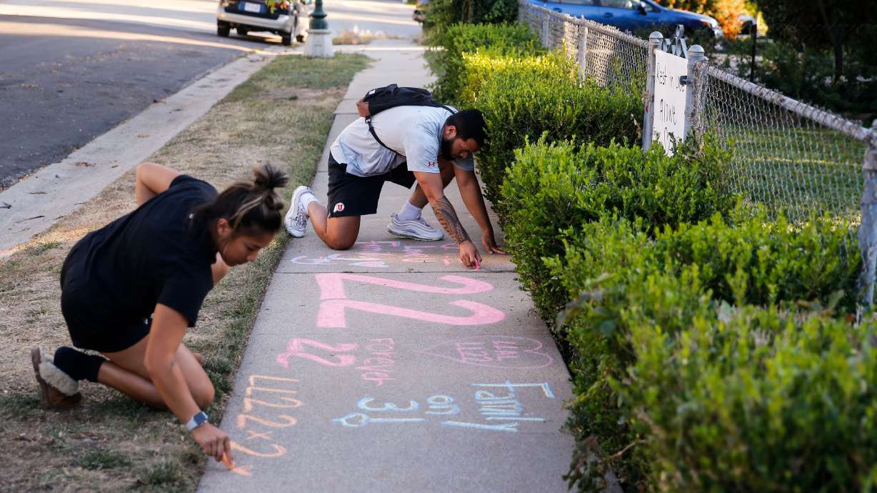 Samuelu Elisaia, back, former University of Utah football player and teammate of sophomore defensive back Aaron Lowe and University of Utah student, Madison Jacobus writes on the sidewalk of a makeshift memorial at the incident of shooting on Sunday in Salt Lake City’s Sugar House neighborhood. University of Utah sophomore and football defensive back Aaron Lowe was shot and killed early Sunday morning during a house party.