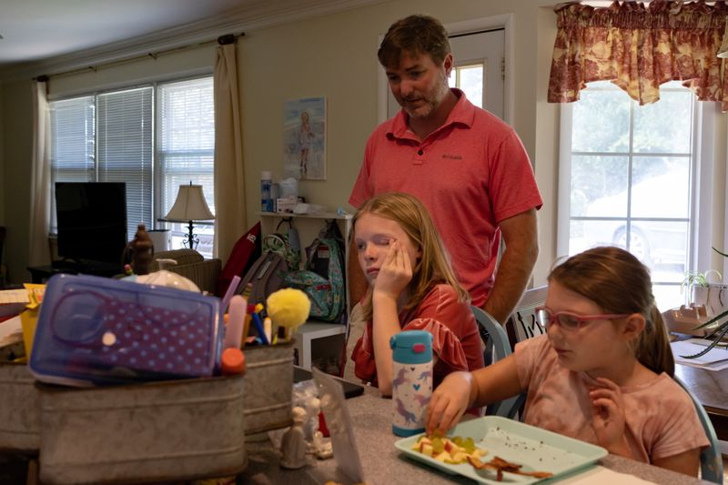 Brian Corley helps his daughter, Anne Grace Corley, 11, with her math homework after making lunch for Ella Rose Corley, 8, who contracted an infection in early childhood that left her legally blind, at their home in Vestavia Hills, Ala., on Sunday.